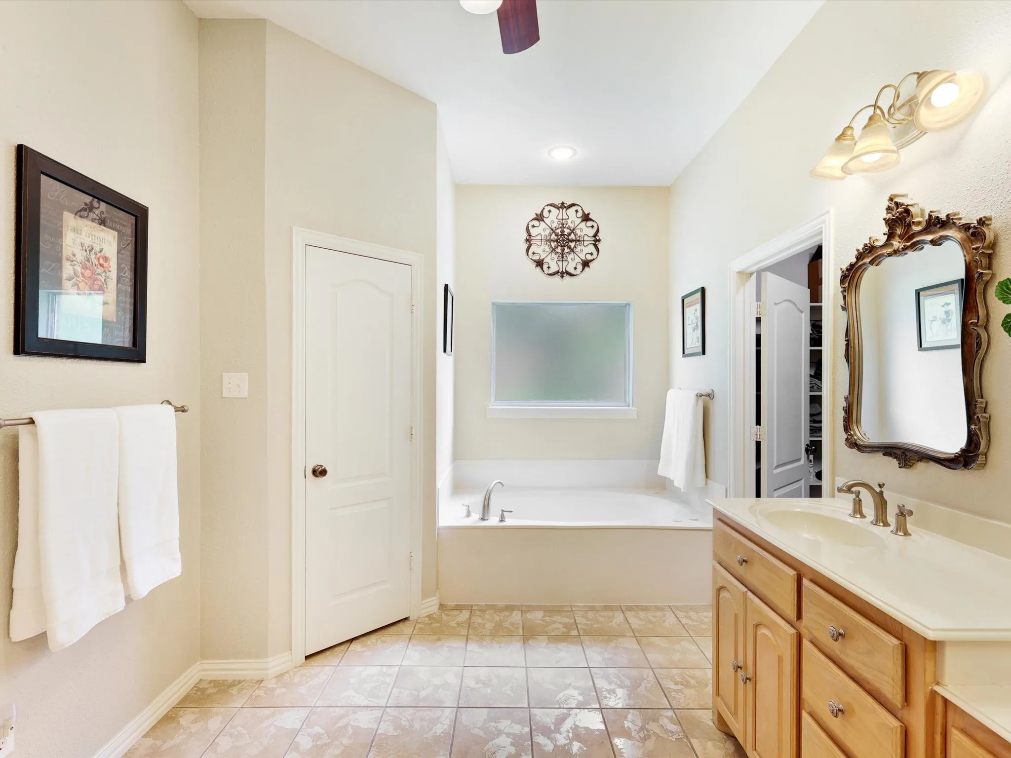 Spacious bathroom featuring a built-in soaking tub, a single vanity with wood cabinetry and a light-toned countertop, and tile flooring