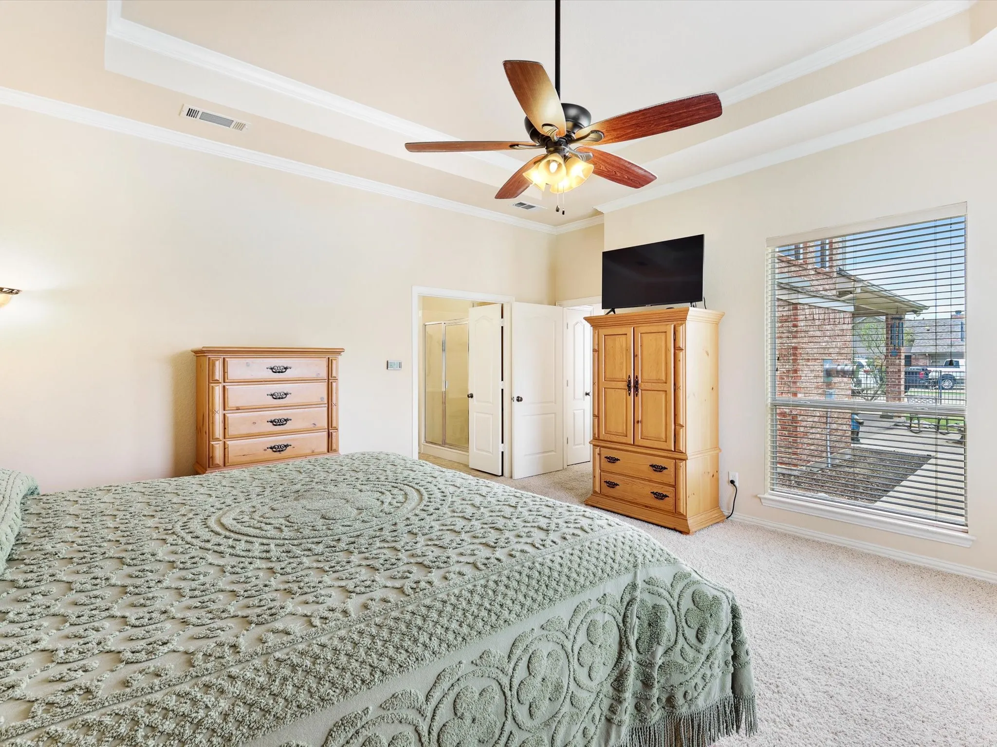 Carpeted room featuring a tray ceiling with crown molding, a ceiling fan with light fixture, and a large window