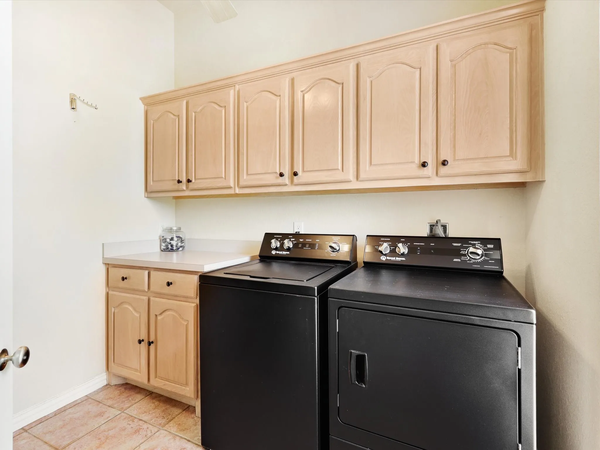 Laundry area featuring upper and lower wood cabinetry, white countertops, and tiled flooring