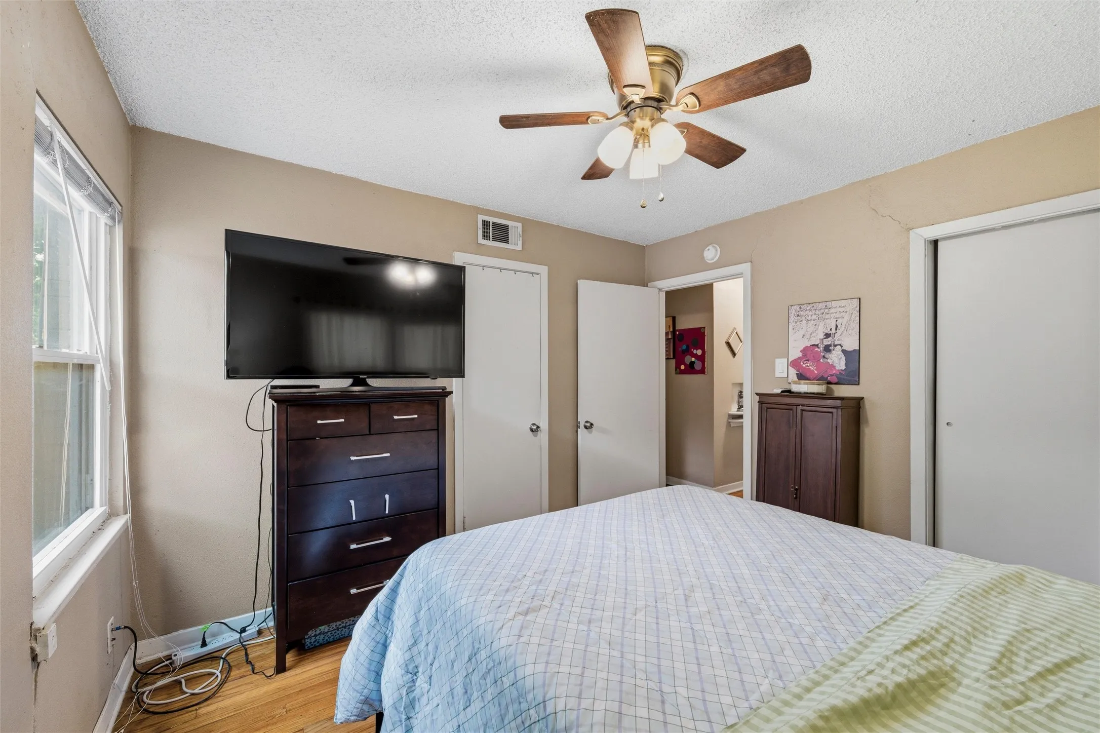 Bedroom features a textured ceiling with ceiling fan and light fixture. Multiple windows provide natural light. Sliding closet doors provide storage. Hardwood flooring extends throughout.