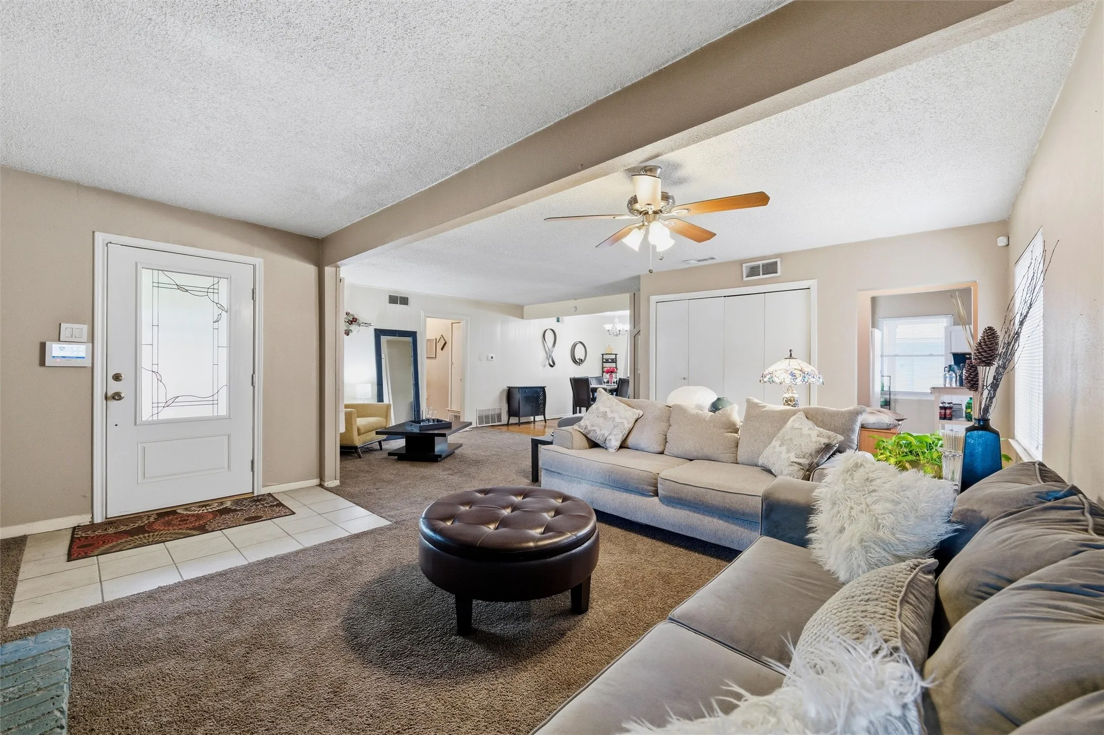Living Room features a textured ceiling with ceiling fan and light fixture. Painted brick fireplace with raised hearth and wood mantel is visible along the side wall. Windows provide natural light. Open layout connects directly to the dining area. Carpet flooring extends throughout.