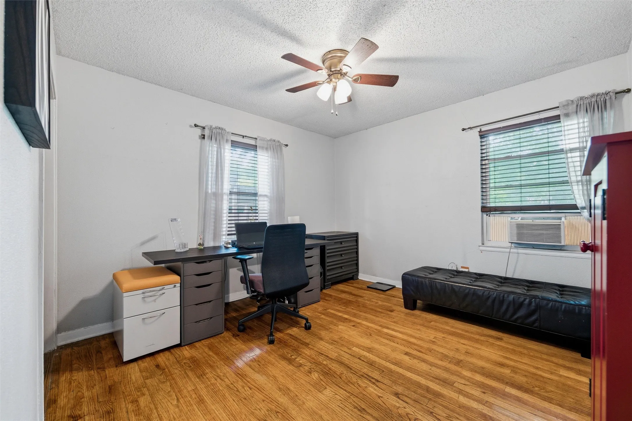 Bedroom features a textured ceiling with ceiling fan and light fixture. Dual windows provide natural light throughout the room. Hardwood flooring extends throughout.