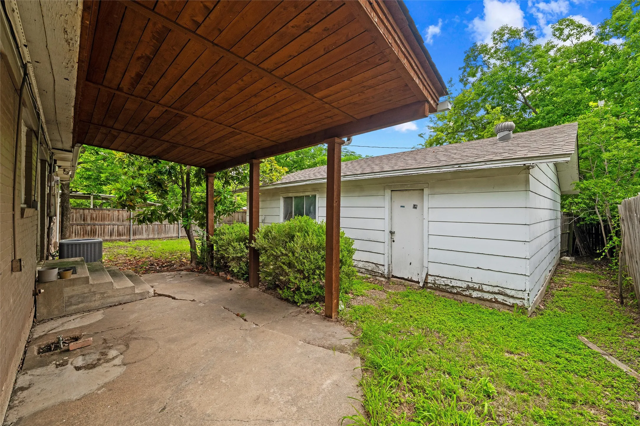 Covered Patio / Backyard features a wood-planked ceiling supported by wood posts. Detached storage building is visible beyond the covered area. Concrete patio surface extends throughout.