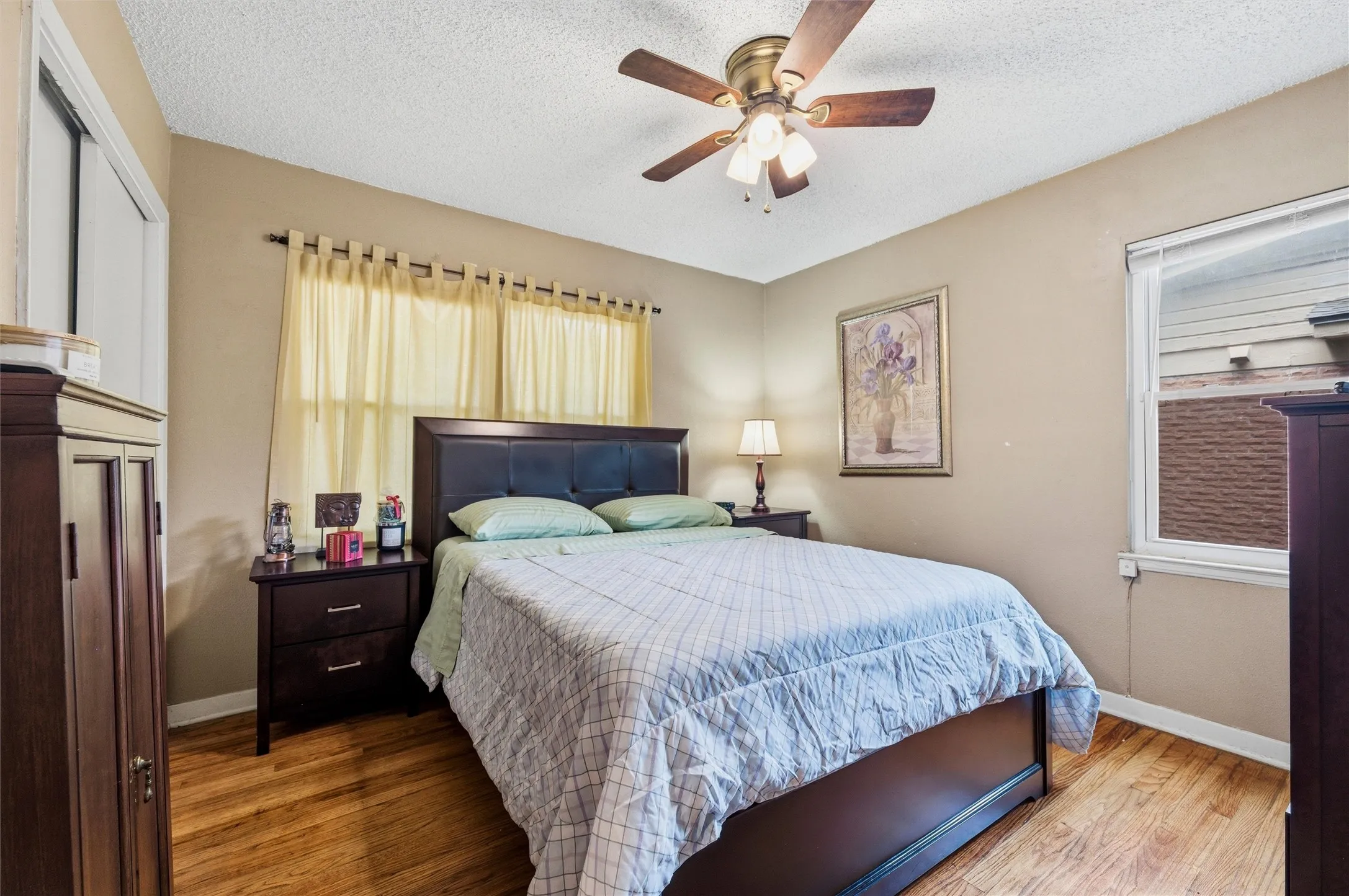 Bedroom features a textured ceiling with ceiling fan and light fixture. Window provides natural light. Sliding closet doors provide storage. Hardwood flooring extends throughout.