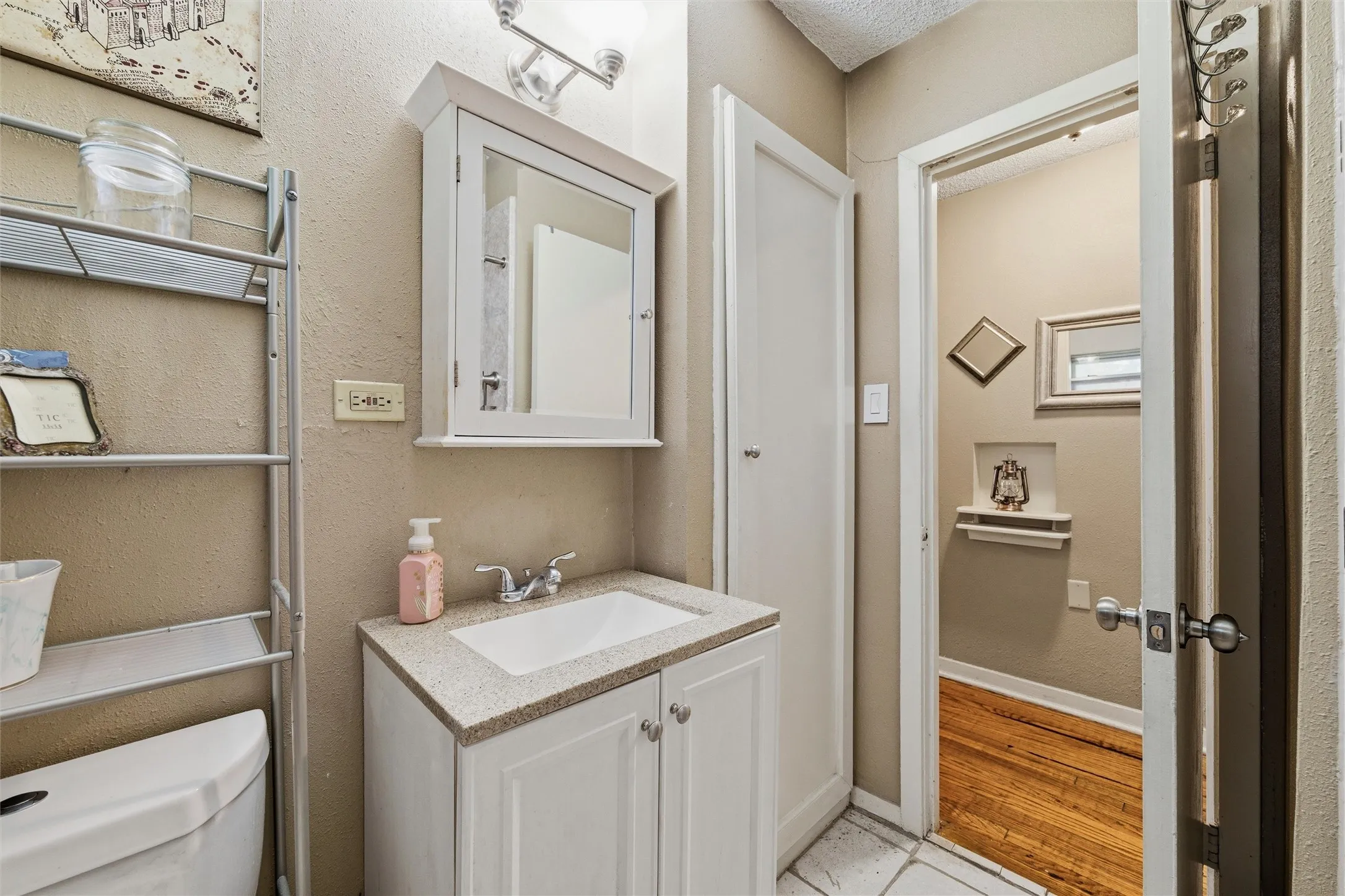 Bathroom features a textured ceiling with vanity lighting. Single-sink vanity includes laminate countertop, undermount sink, and medicine cabinet with mirror. Walk-in shower is positioned adjacent to the vanity. Tile flooring extends throughout.