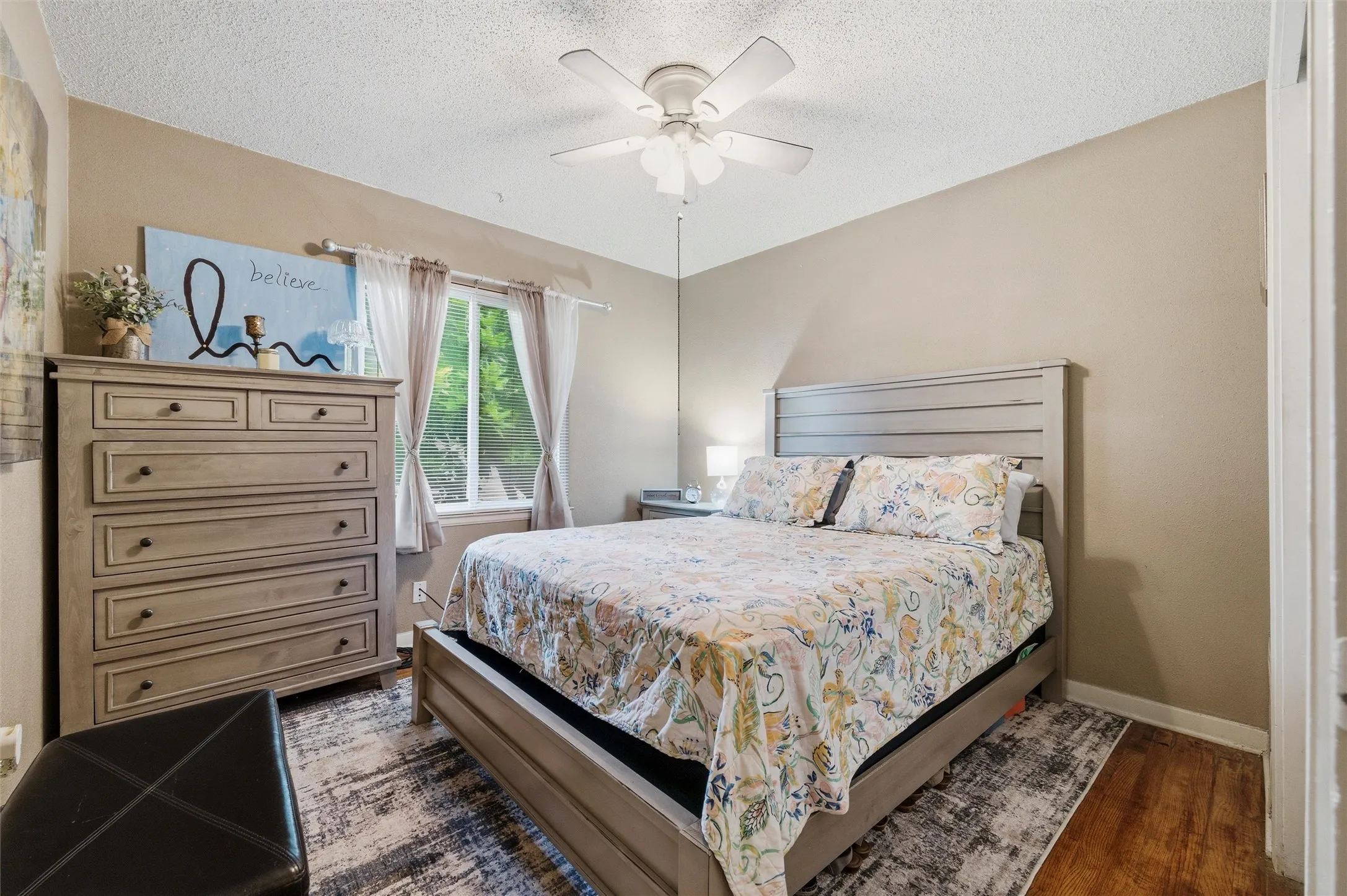 Bedroom features a textured ceiling with ceiling fan and light fixture. Sliding closet doors provide storage. Window provides natural light. Hardwood flooring extends throughout.