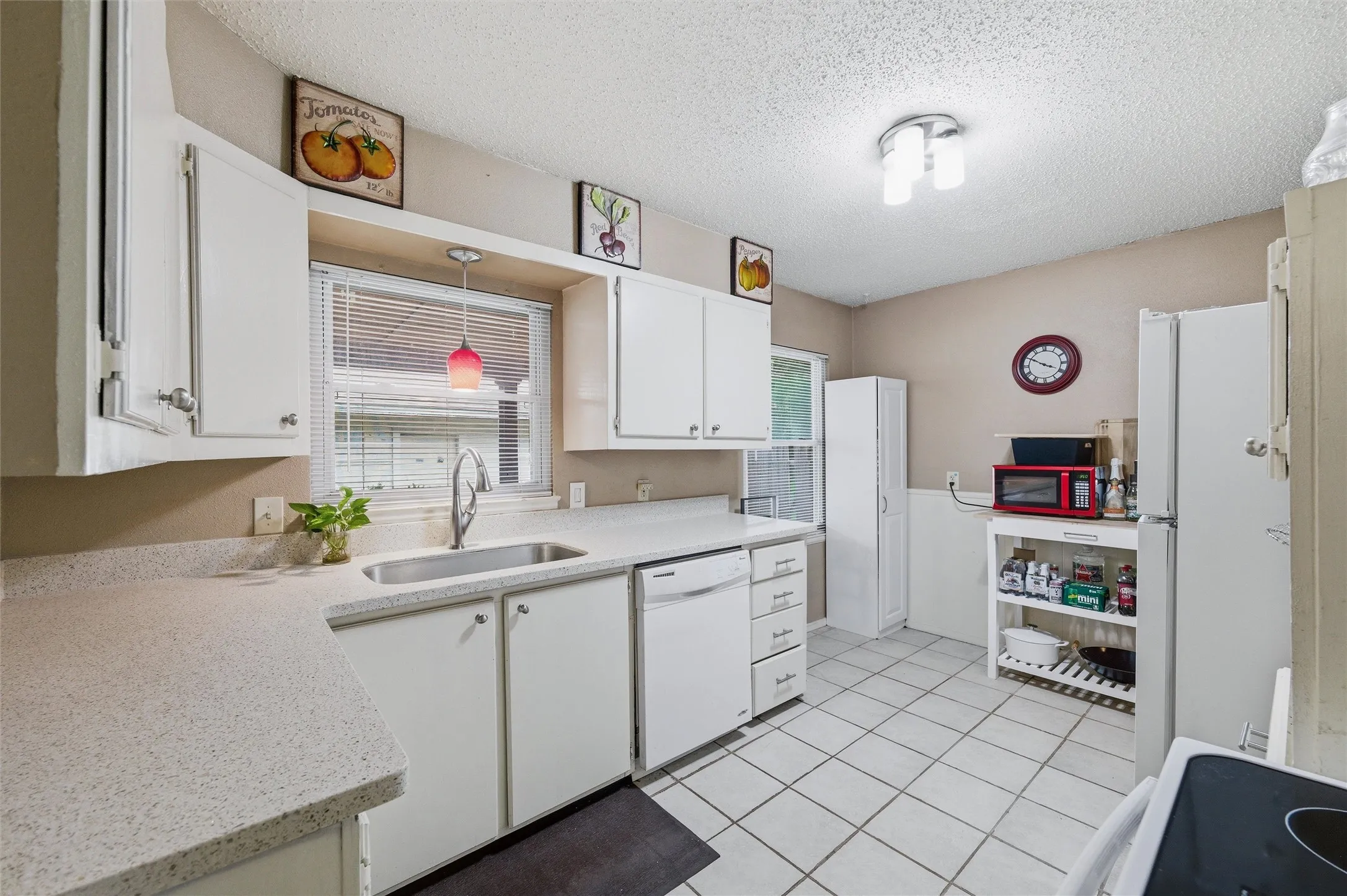 Kitchen features a textured ceiling with flush-mount light fixture and pendant lighting above the sink. White raised-panel cabinetry extends throughout with laminate countertops and single-basin sink. Appliances include an electric range and dishwasher. Tile flooring extends throughout.