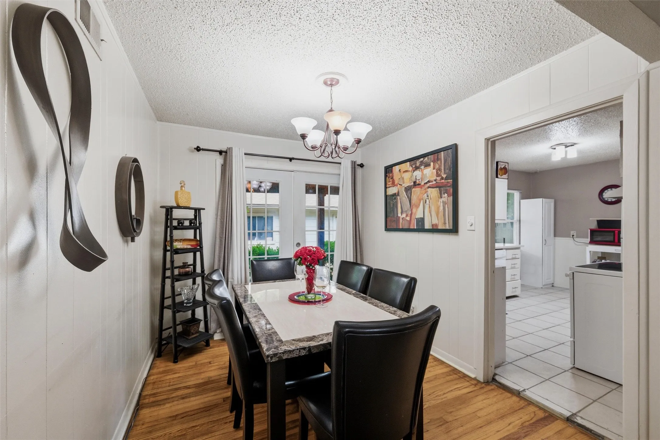 Dining Area features a textured ceiling with chandelier light fixture. Vertical board wall paneling extends throughout the room. French doors provide natural light and exterior access. Hardwood flooring extends throughout.