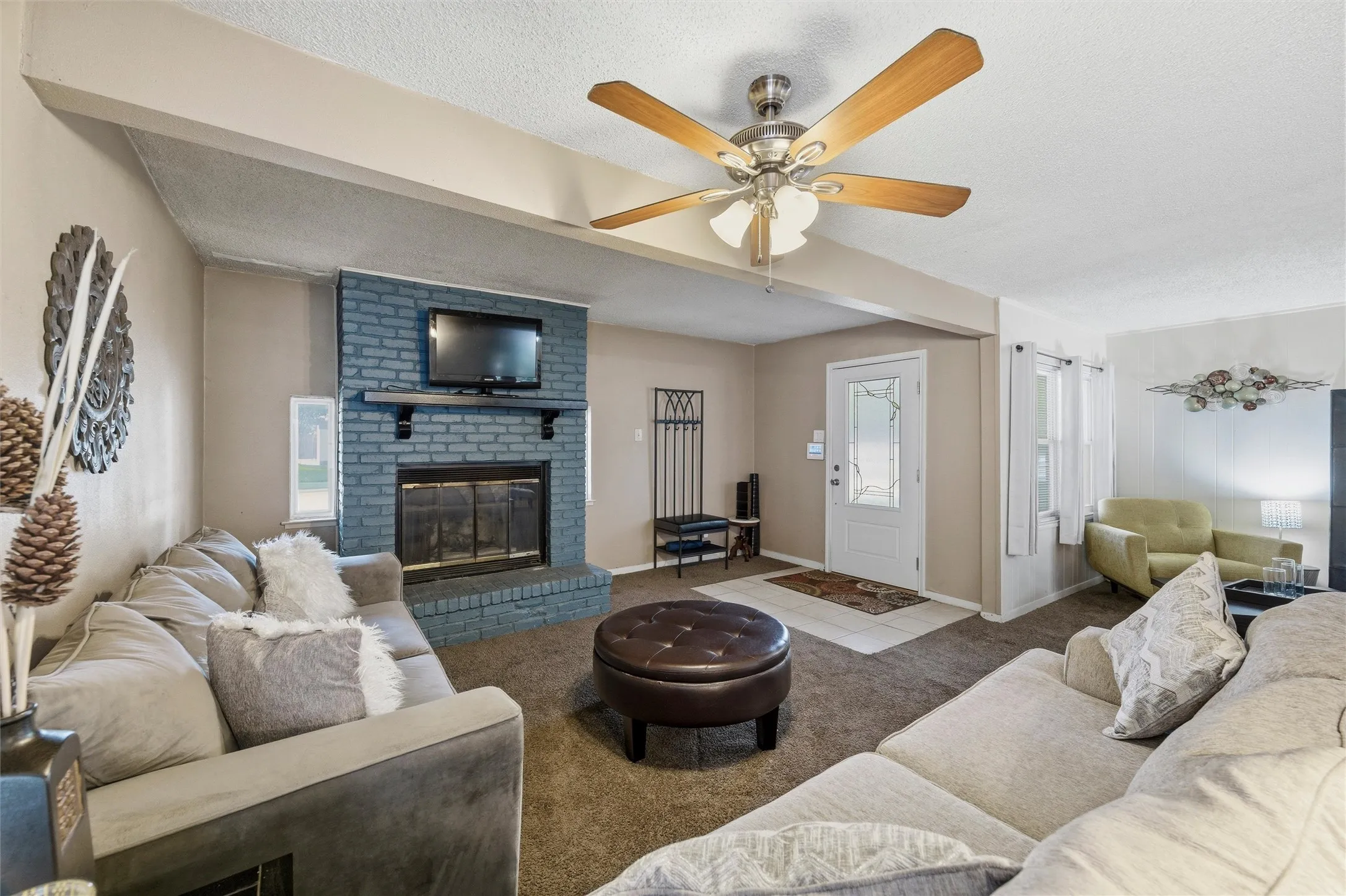 Living Room features a textured ceiling with ceiling fan and light fixture. Entry door includes decorative glass insert. Open layout connects directly to the dining area and hallway. Storage closet with bi-fold doors is positioned along the interior wall. Carpet flooring extends throughout with tile flooring at the entry.