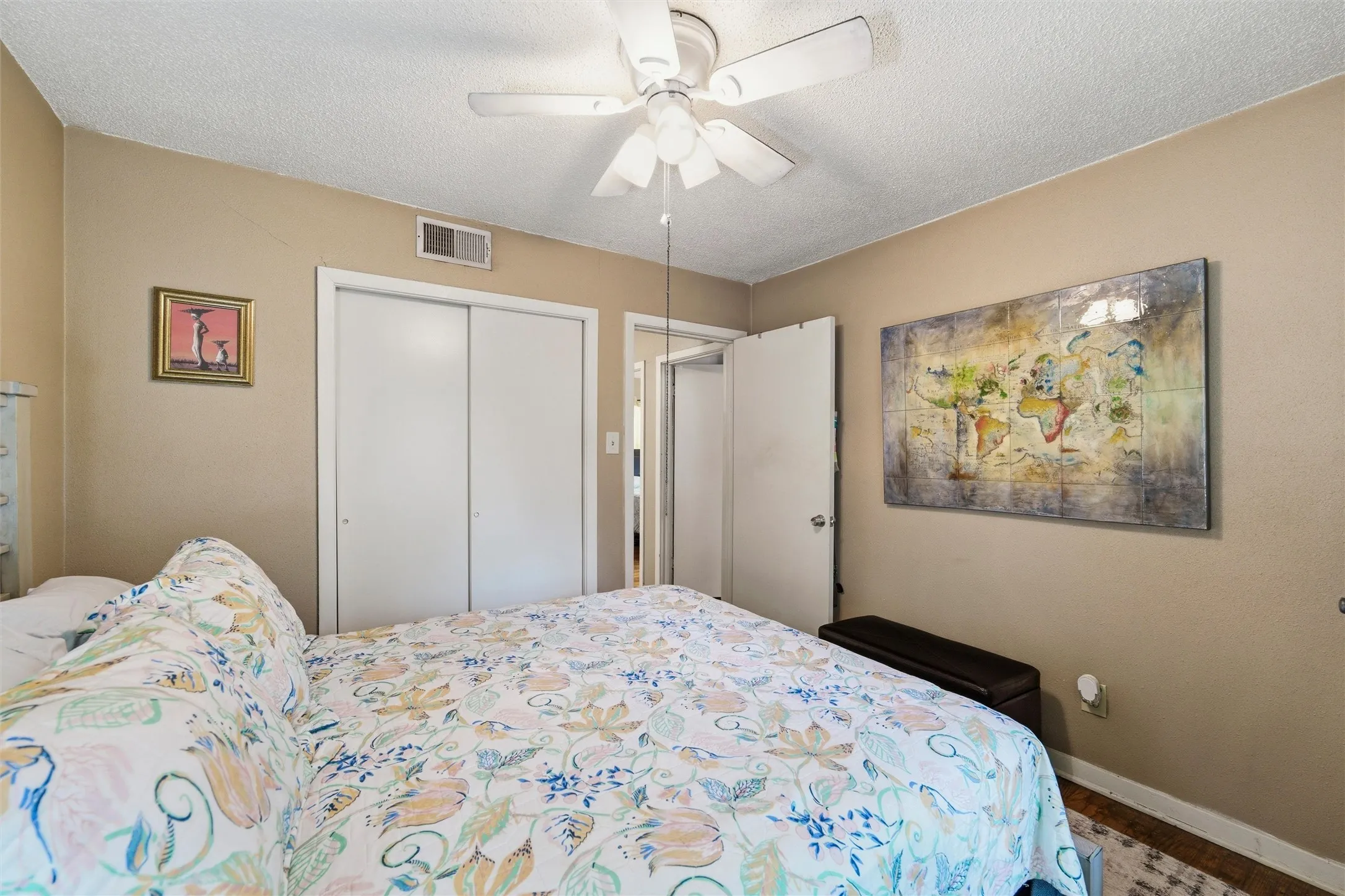 Bedroom features a textured ceiling with ceiling fan and light fixture. Window provides natural light. Sliding closet doors provide storage. Hardwood flooring extends throughout.