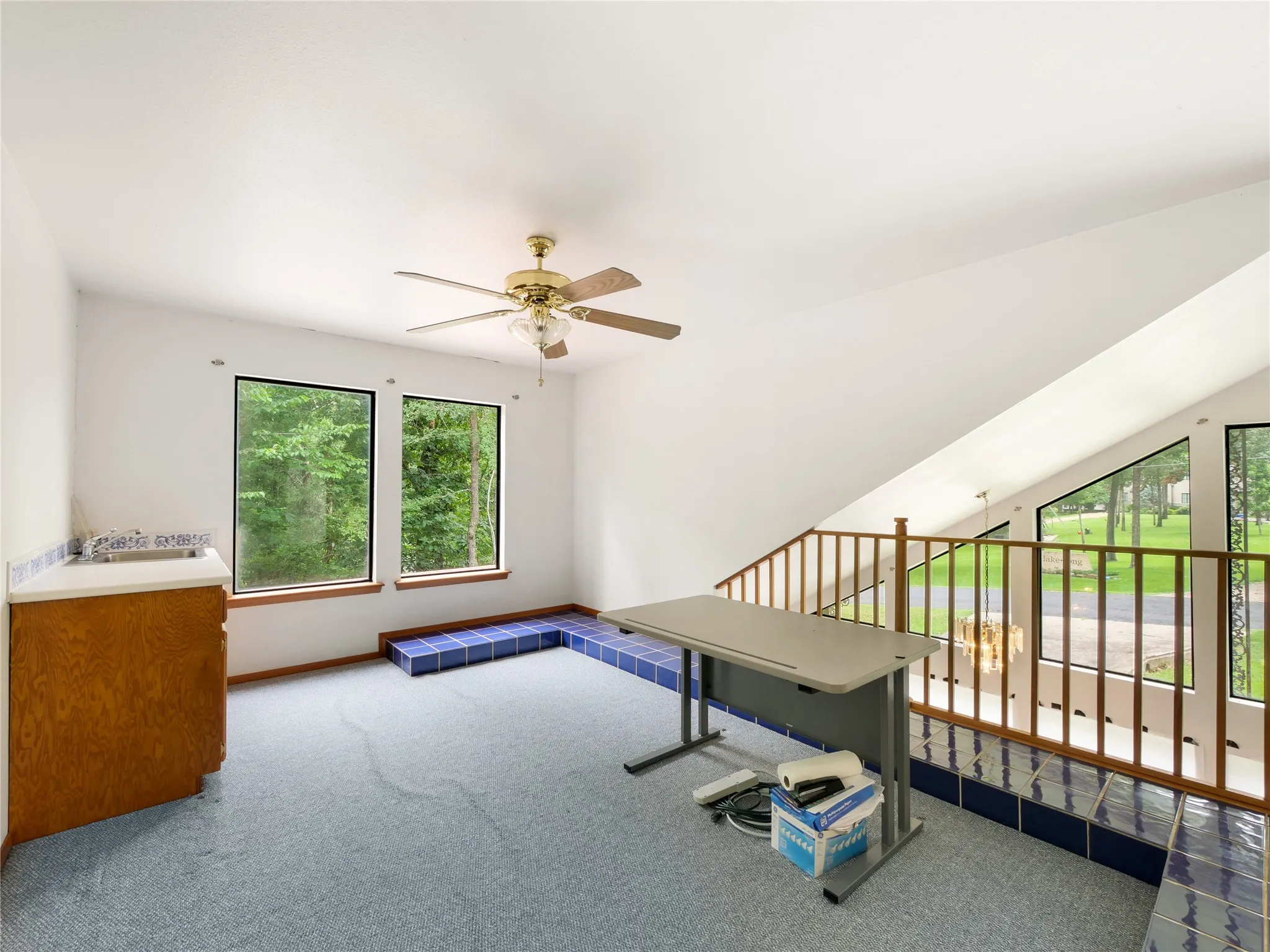Carpeted loft area featuring a ceiling fan, a built-in wet bar with a tiled countertop, and multiple windows