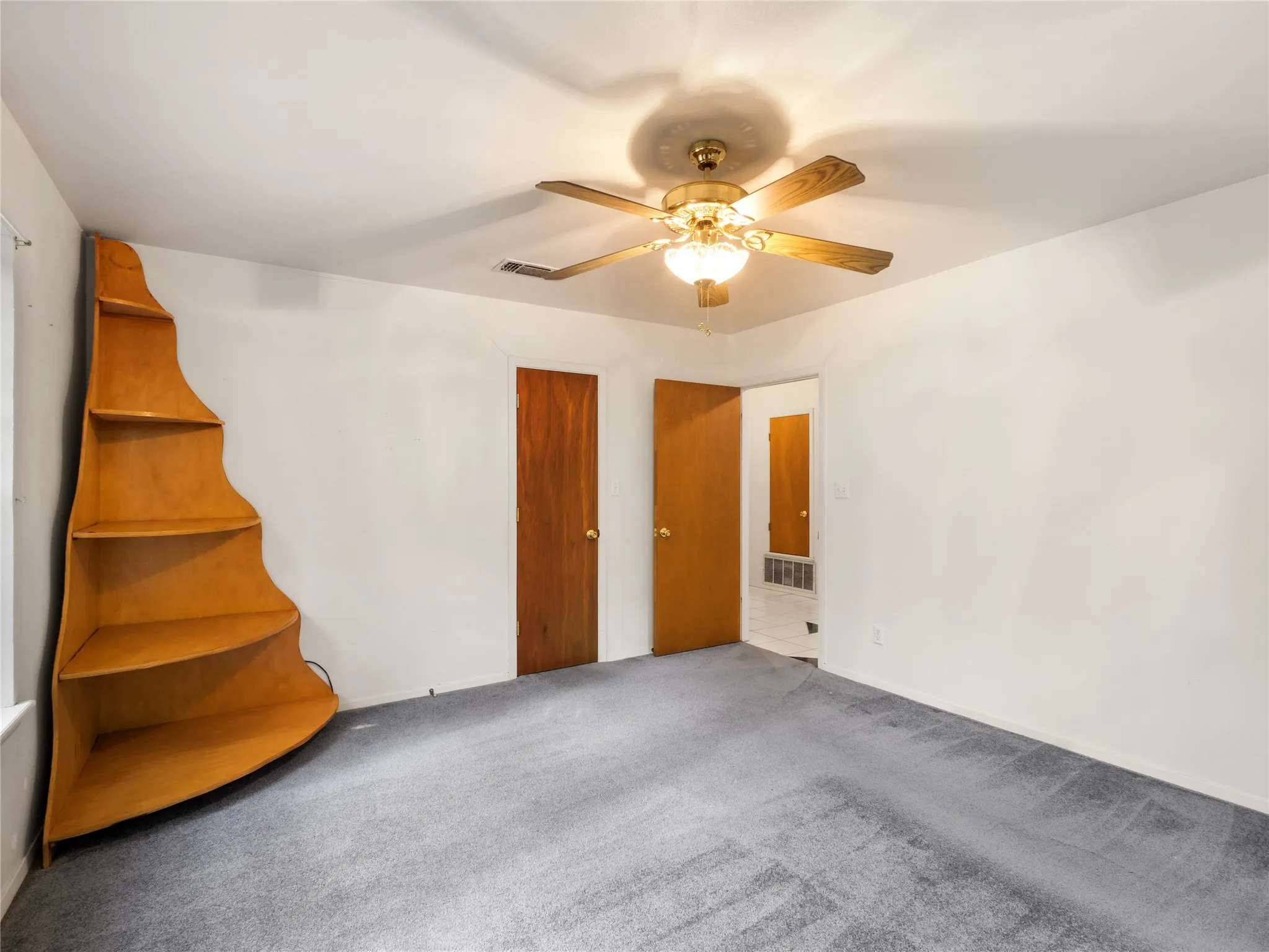 Spacious room featuring light gray carpet, white walls, and a ceiling fan with integrated lighting