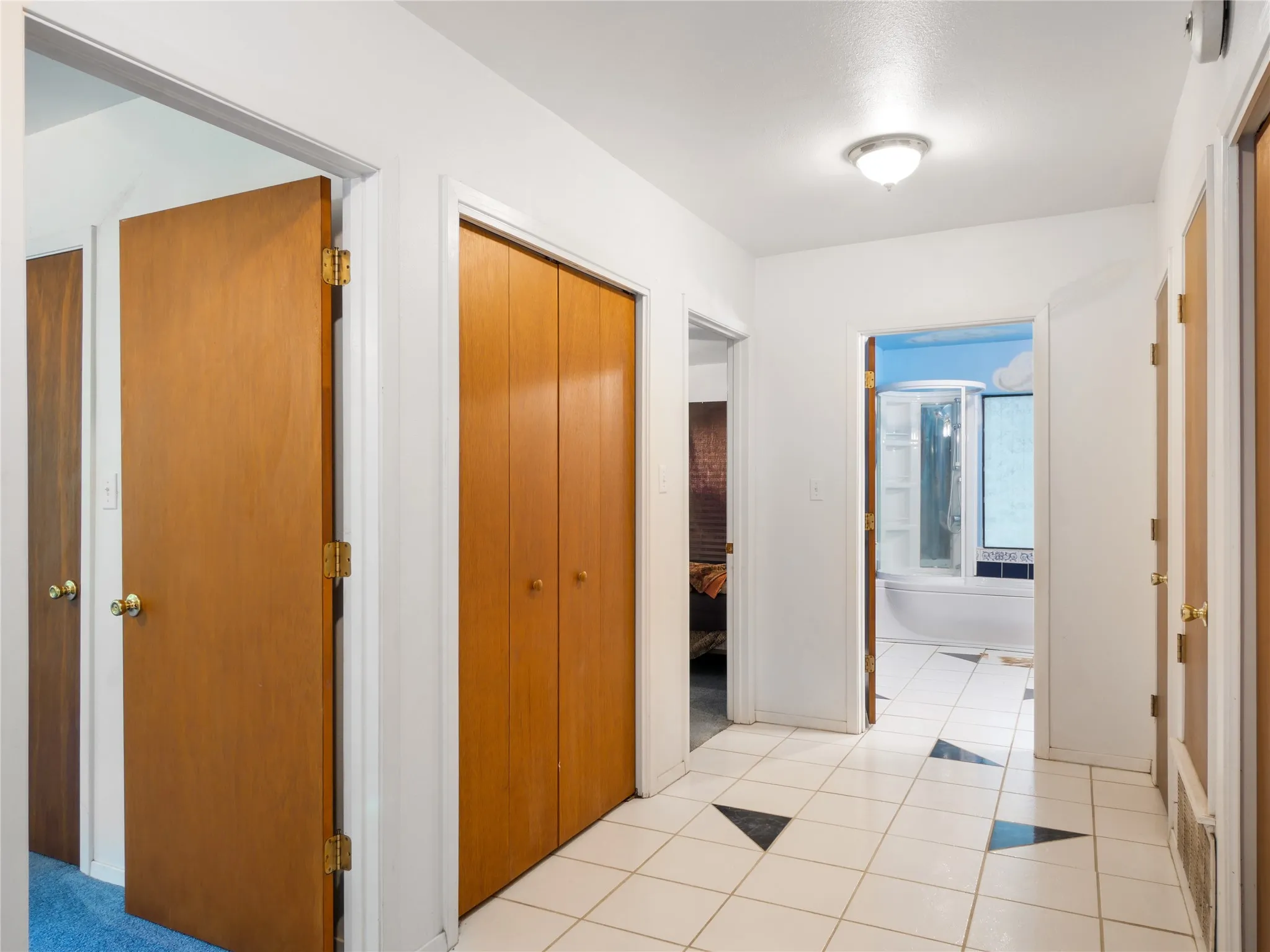 Hallway featuring ceramic tile flooring with black geometric accents, multiple wood-finish doors, and a flush mount ceiling light