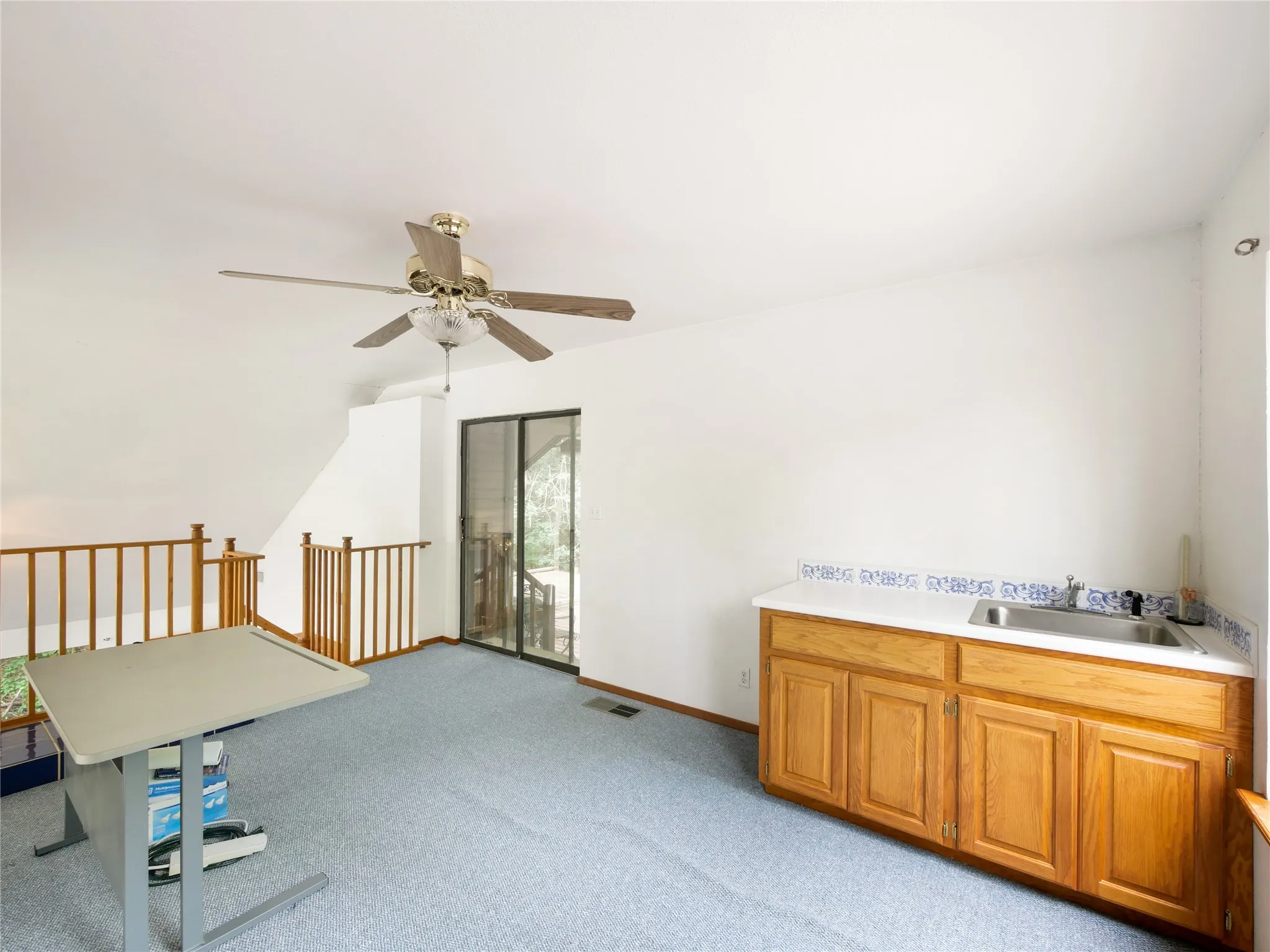 Carpeted loft area featuring a ceiling fan, a built-in wet bar with a tiled countertop, and multiple windows
