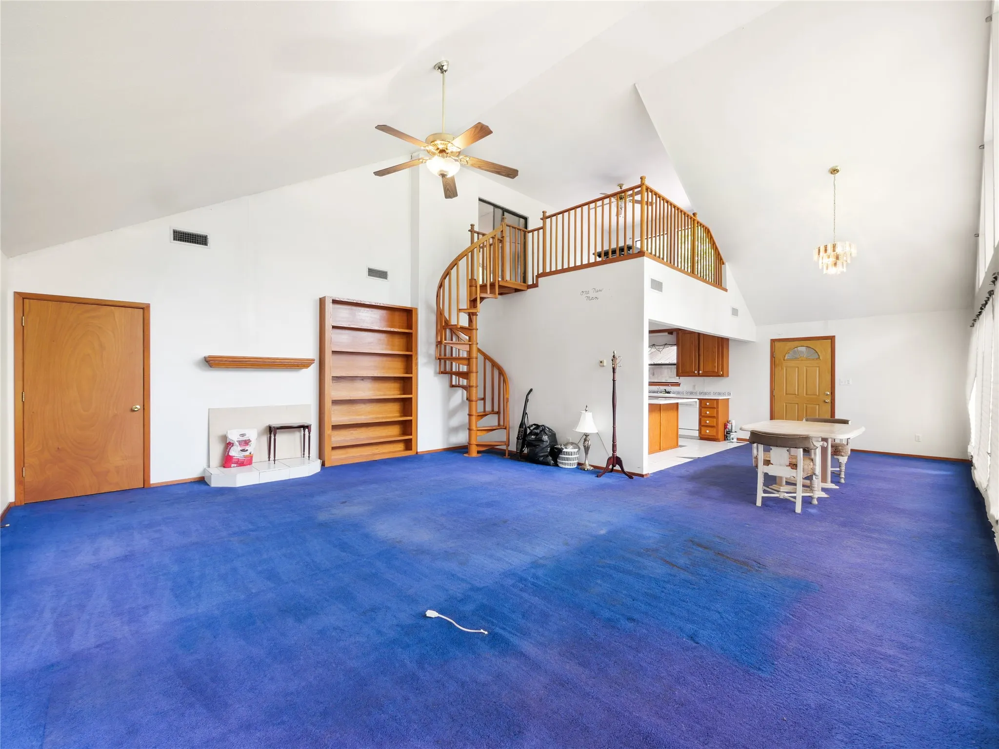 Spacious room featuring vaulted ceilings, a spiral staircase with wood newels and balusters, built-in wooden shelving, an integrated fireplace, and a ceiling fan