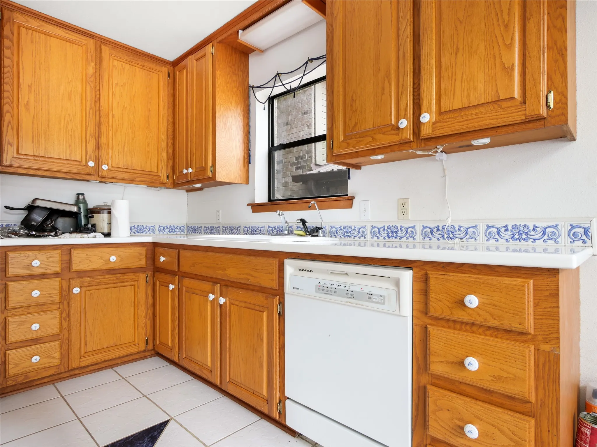 Warm wood cabinetry, white countertops, a mosaic tile backsplash, and a white built-in dishwasher