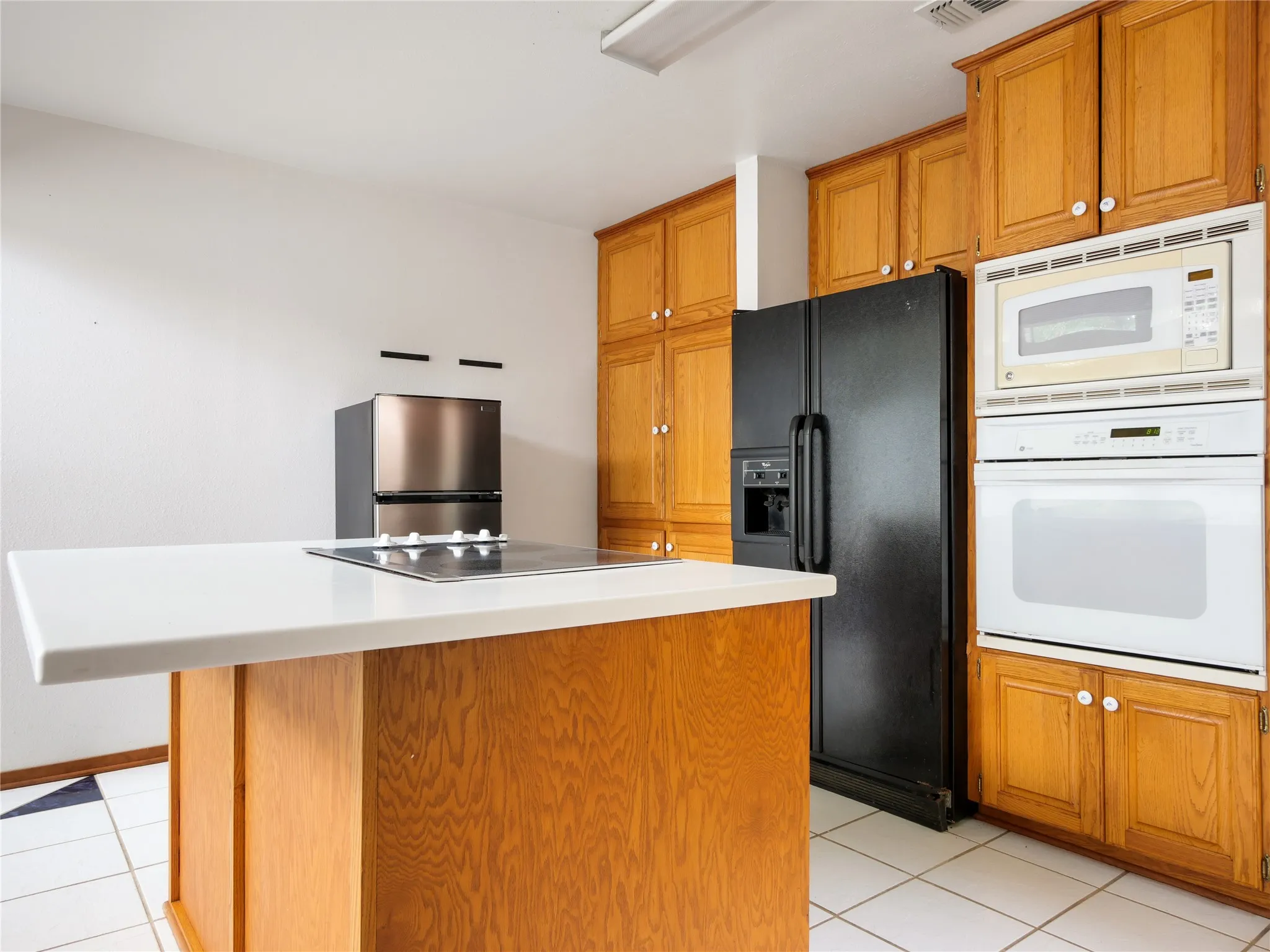 Kitchen island with a white solid surface countertop and built-in electric cooktop, complemented by natural wood-finish cabinetry