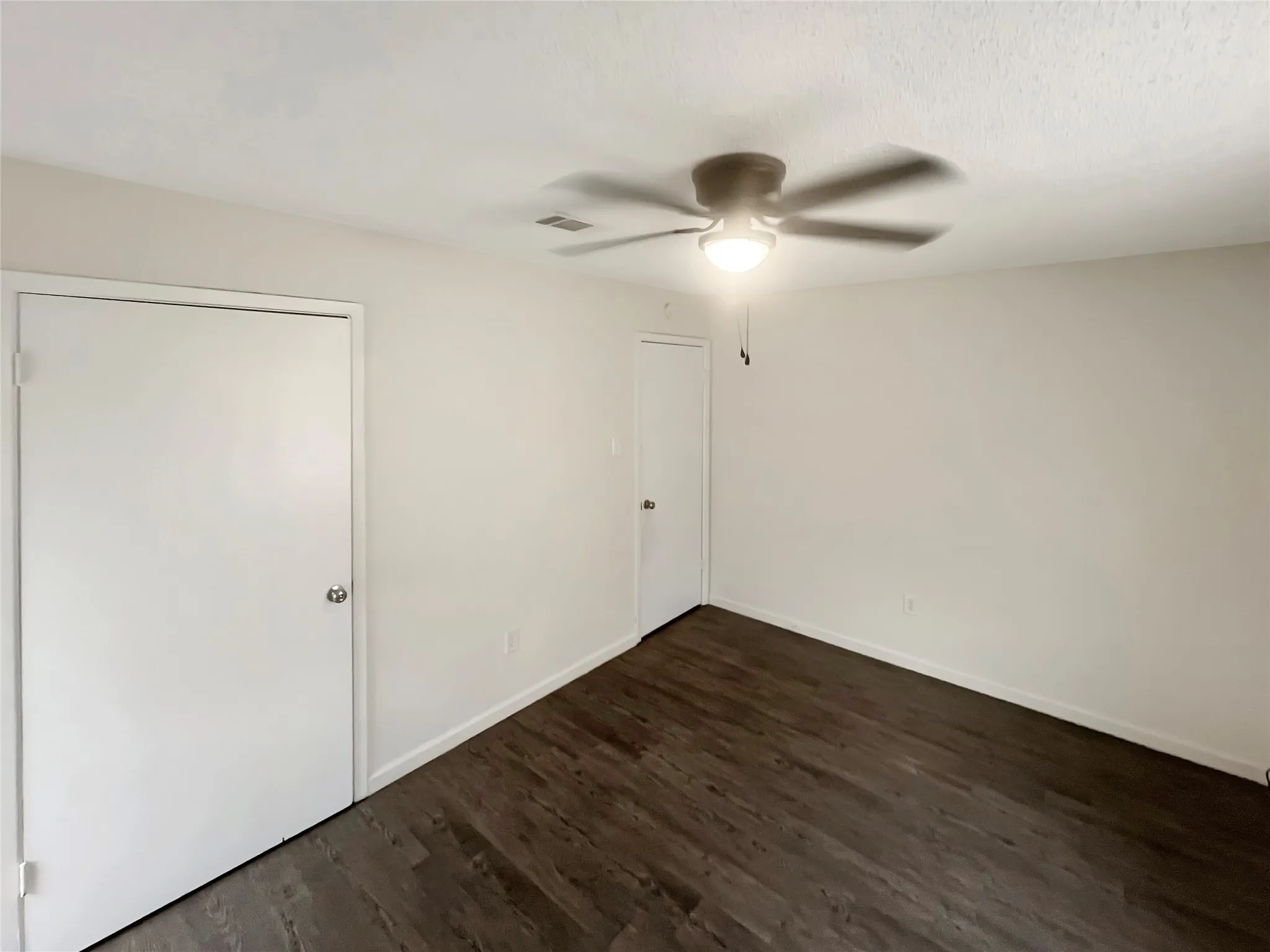 Spacious room featuring wood-finish flooring, white walls, and a ceiling fan with integrated lighting