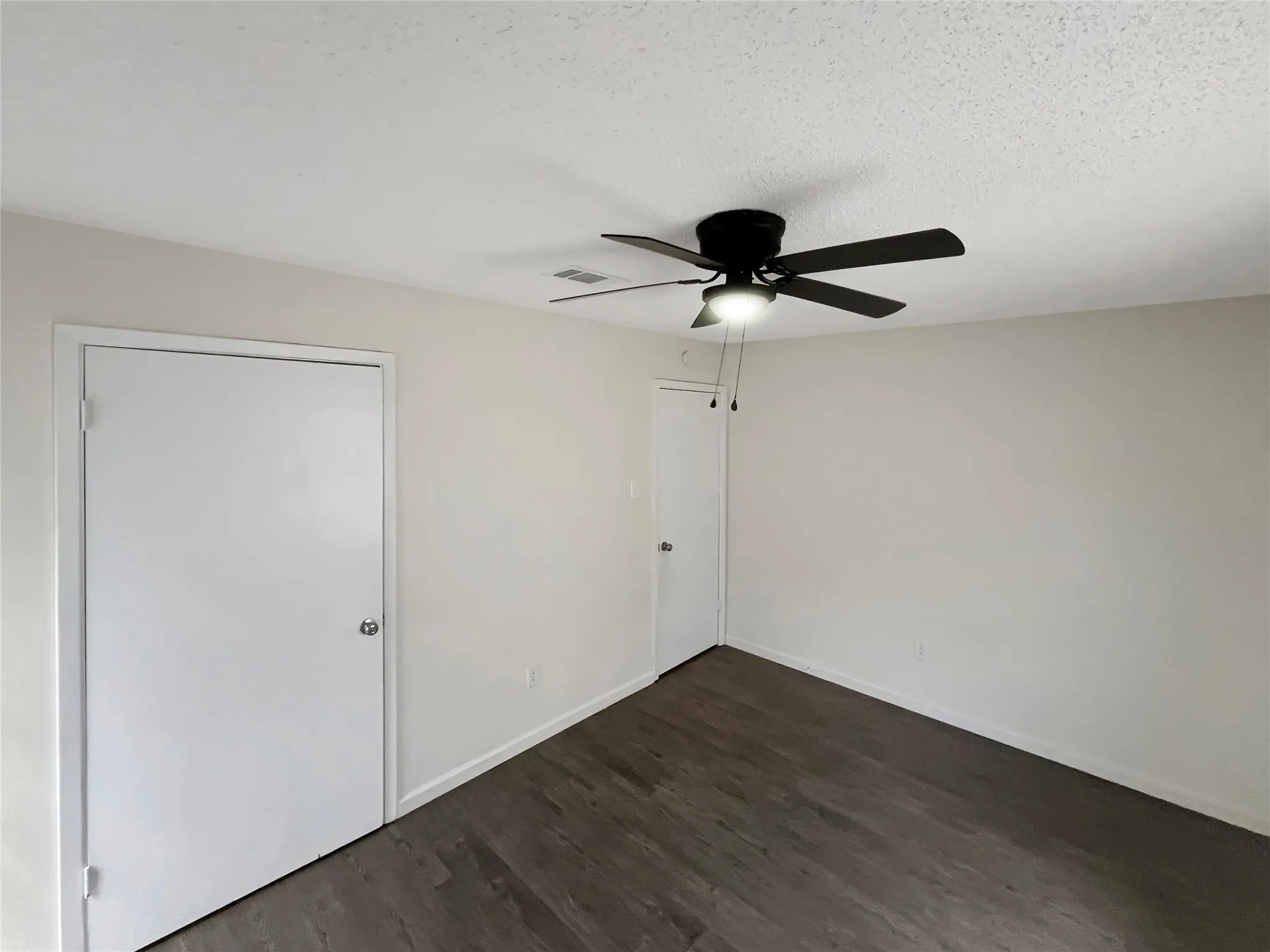 Spacious room featuring wood-finish flooring, light-toned walls, and a ceiling fan with integrated lighting
