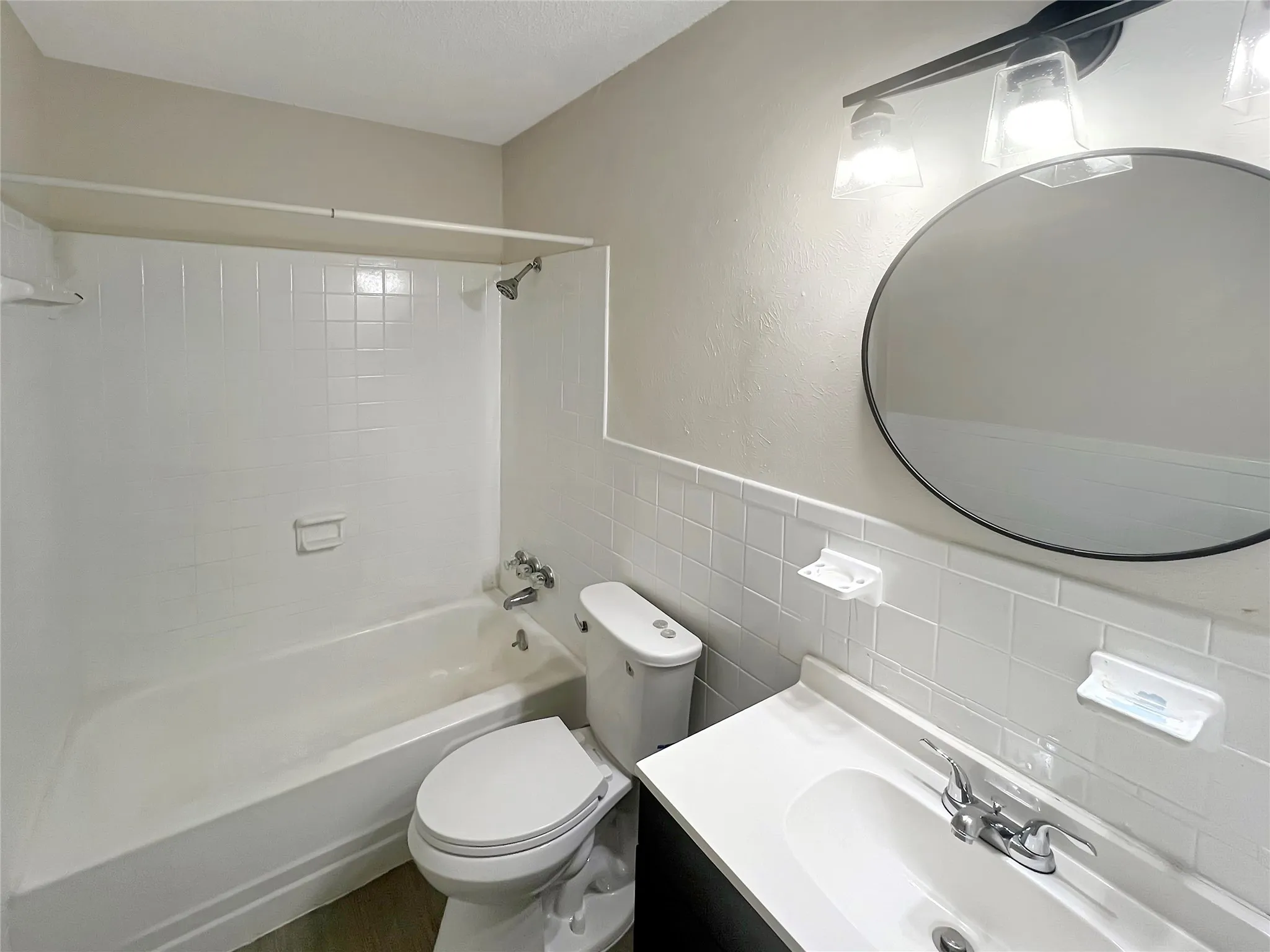 Bathroom featuring a white subway tile wainscoting, a white vanity countertop with an integrated sink, a circular mirror with a black frame, and a matte black two-light vanity fixture