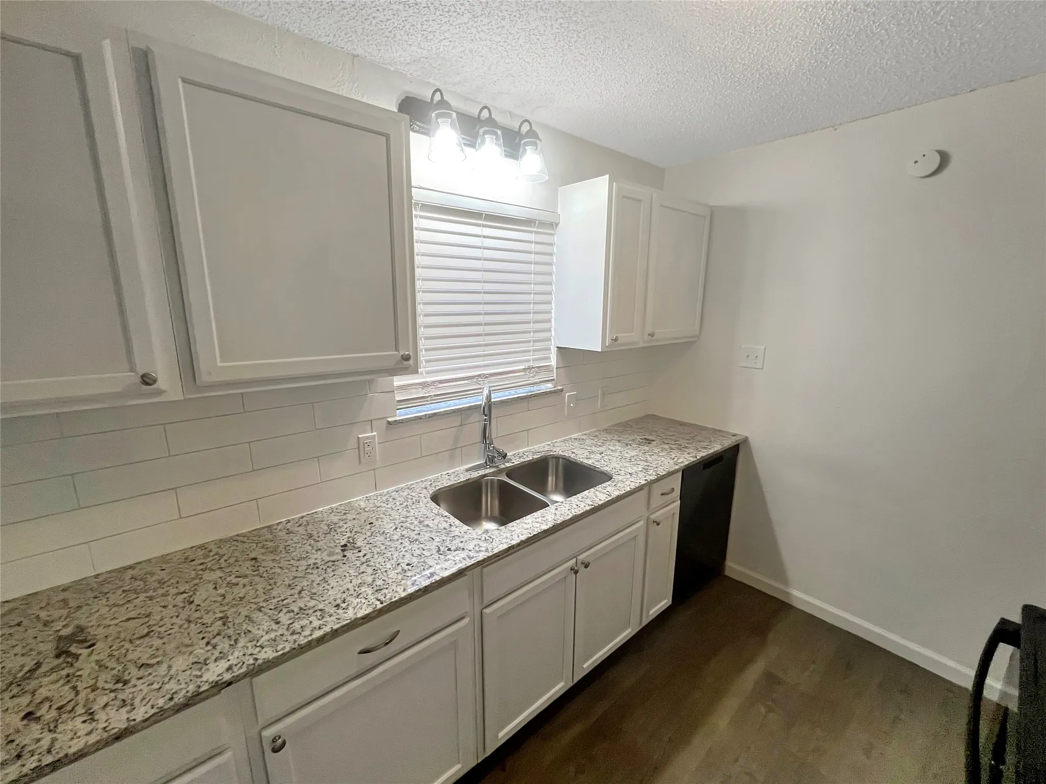 Kitchen featuring white cabinetry, light-toned patterned countertops, subway tile backsplash, a double basin stainless steel sink with a chrome faucet, and wood-finish flooring