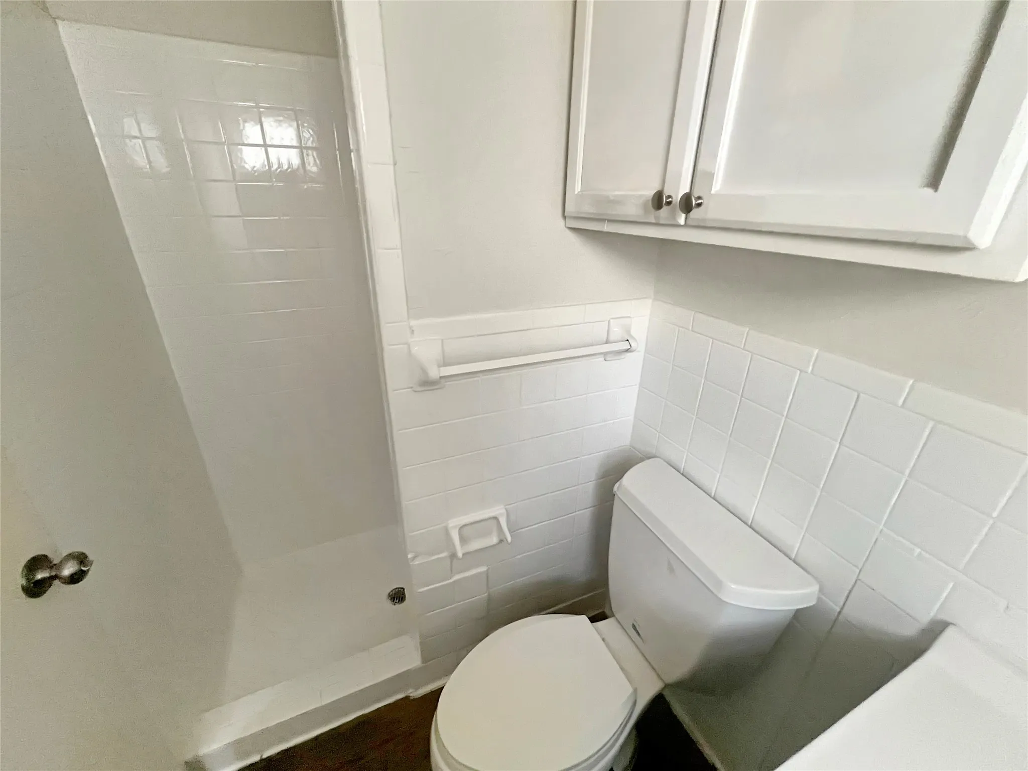 Bathroom featuring white subway tile wainscoting, white wall-mounted cabinetry, and a white toilet