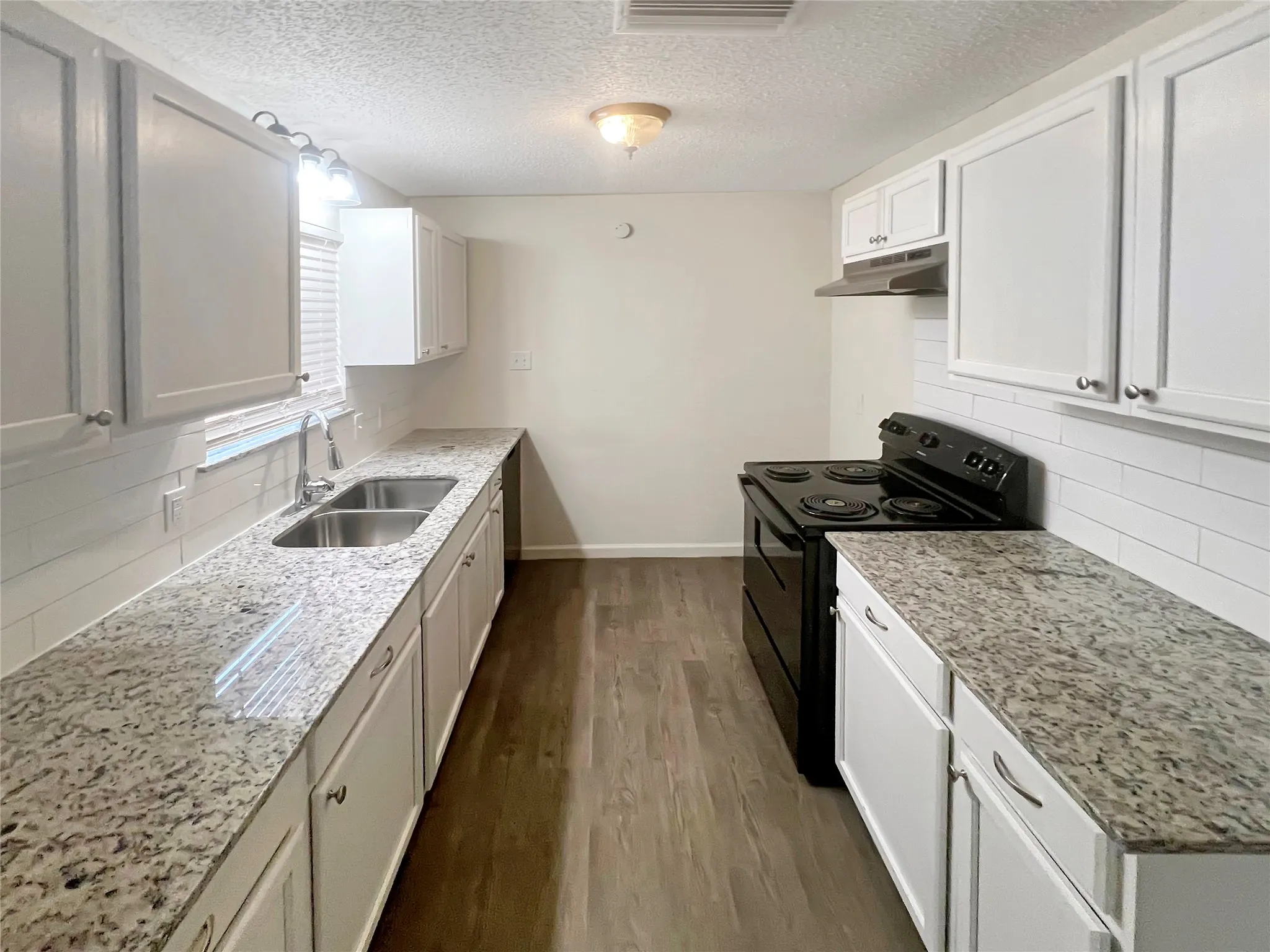 Modern kitchen featuring white shaker cabinetry, granite countertops, white subway tile backsplash, a double basin stainless steel sink, and wood-finish flooring