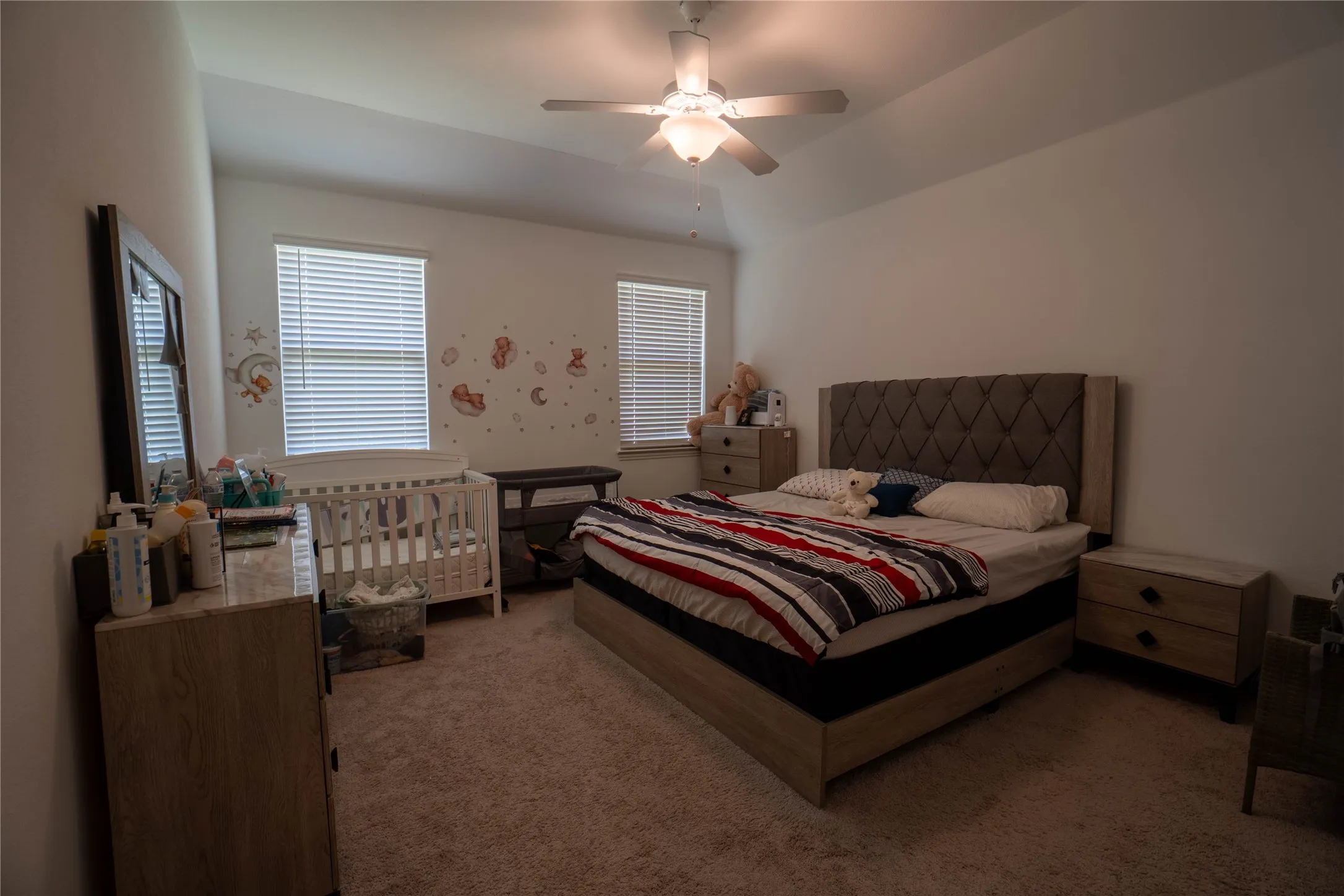Spacious bedroom featuring a tray ceiling, ceiling fan with integrated lighting, twin windows with blinds, and carpeted flooring