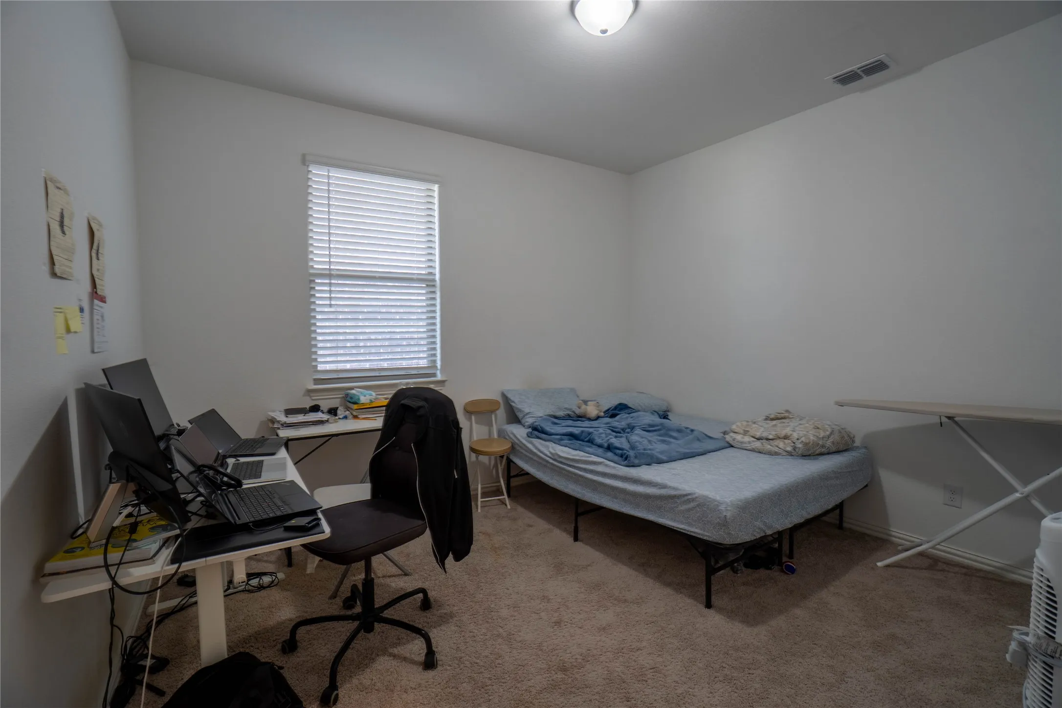 Light-filled room featuring neutral carpet flooring, a single window with horizontal blinds, and a flush-mount ceiling light fixture