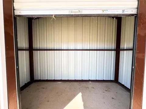 Interior storage unit featuring a roll-up door, corrugated metal walls, and a concrete floor