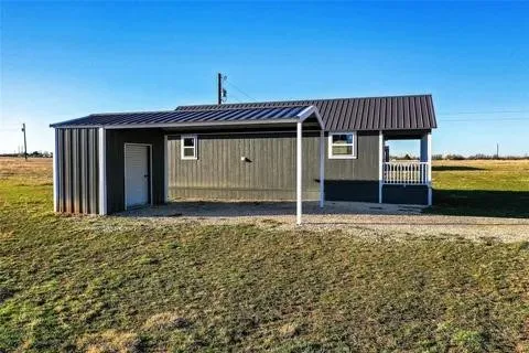 Property exterior featuring a dark gray corrugated metal roof, gray vertical siding, and a covered porch with white railings