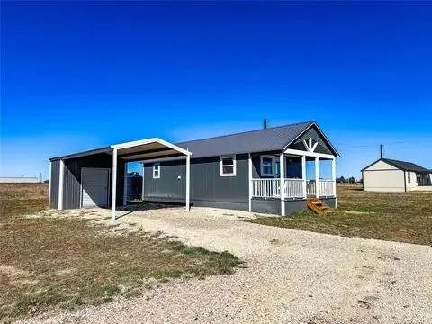 Gray manufactured home featuring a covered front porch with white railing, a dark gray metal roof, and a gravel driveway