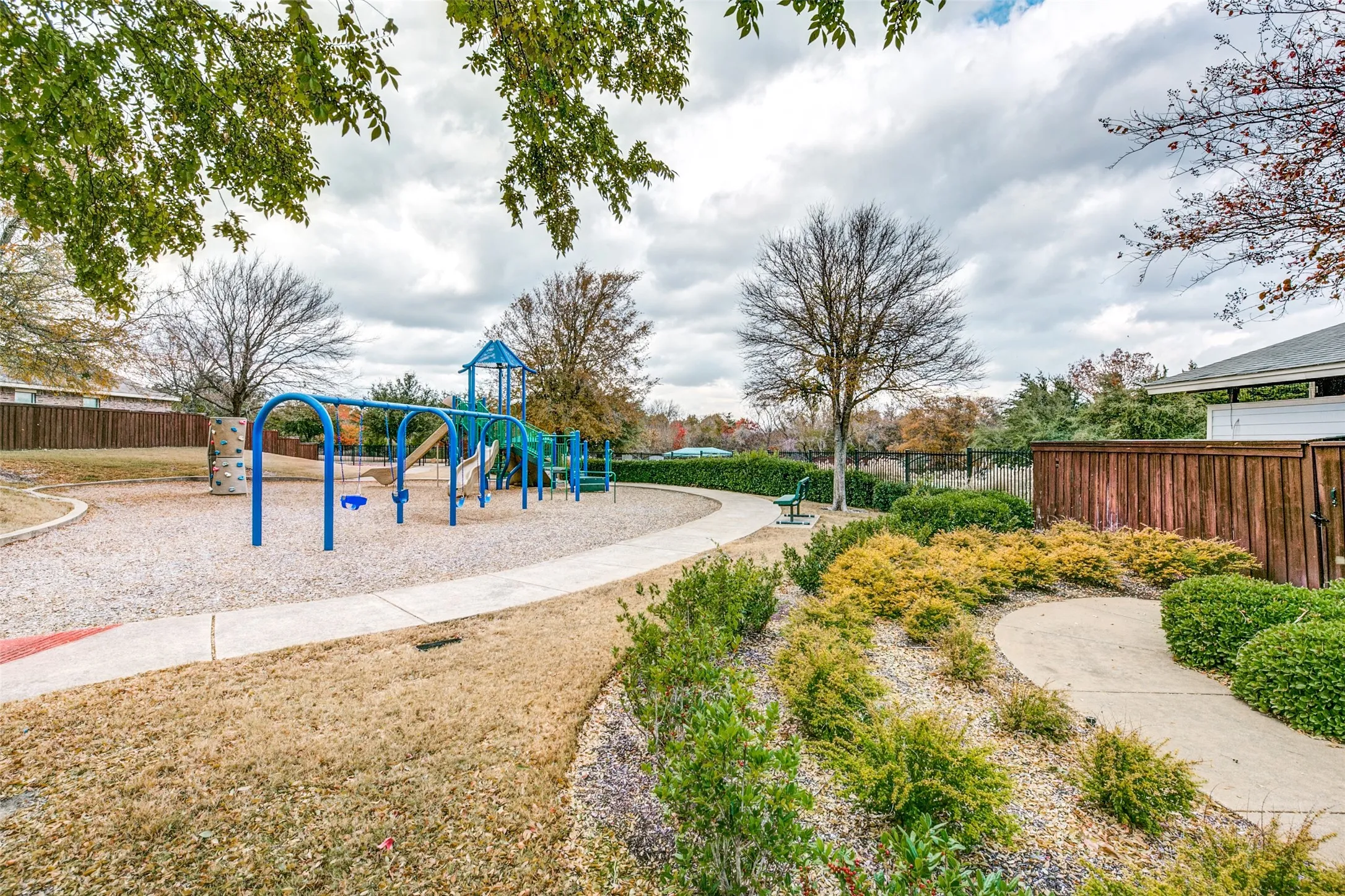 Outdoor recreational area featuring a playground with blue and green equipment, a climbing wall, and swings