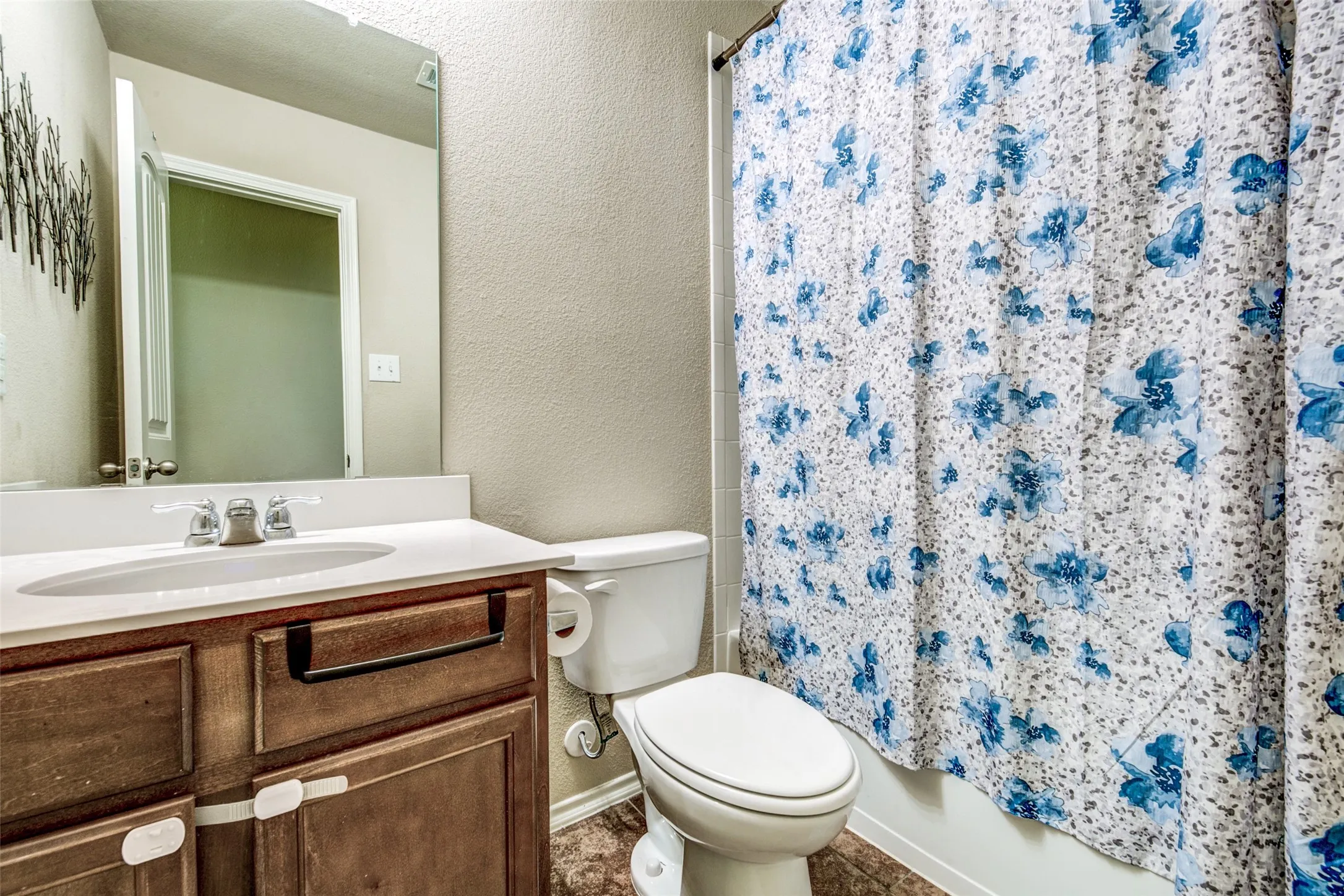 Bathroom featuring a wood-finish vanity with a white countertop and integrated sink, a large wall-mounted mirror, a commode, and a shower with a privacy curtain