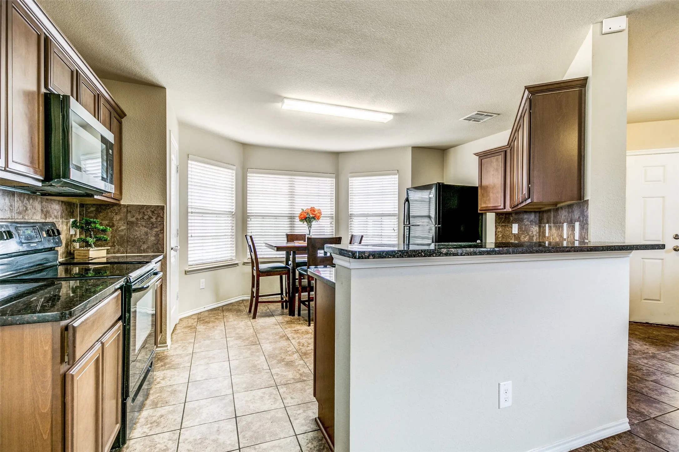 Kitchen featuring wood cabinetry, dark countertops, tiled backsplash, and stainless steel appliances