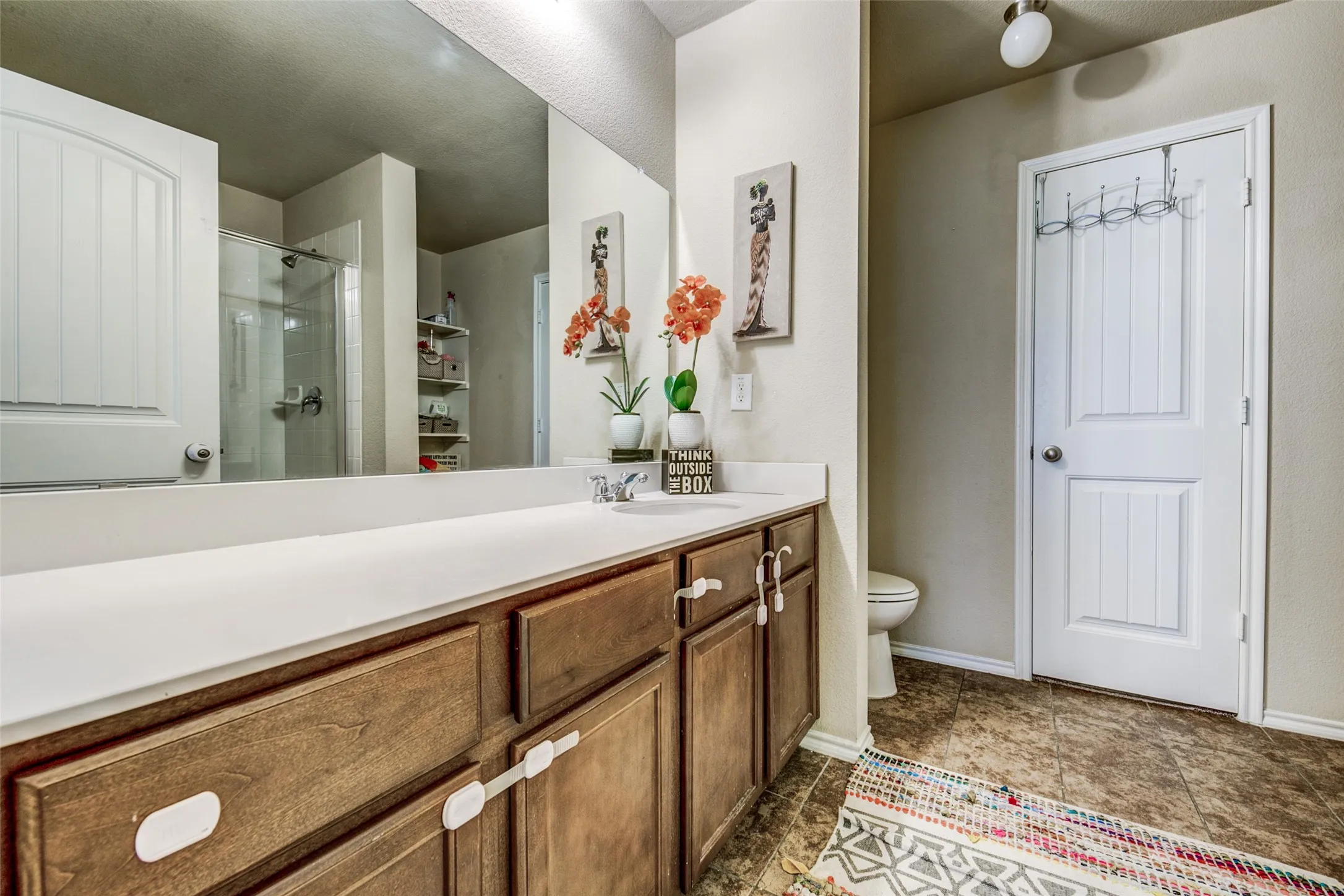 Vanity featuring dual sinks with a white countertop, wood-finish cabinetry, and a large wall-mounted mirror