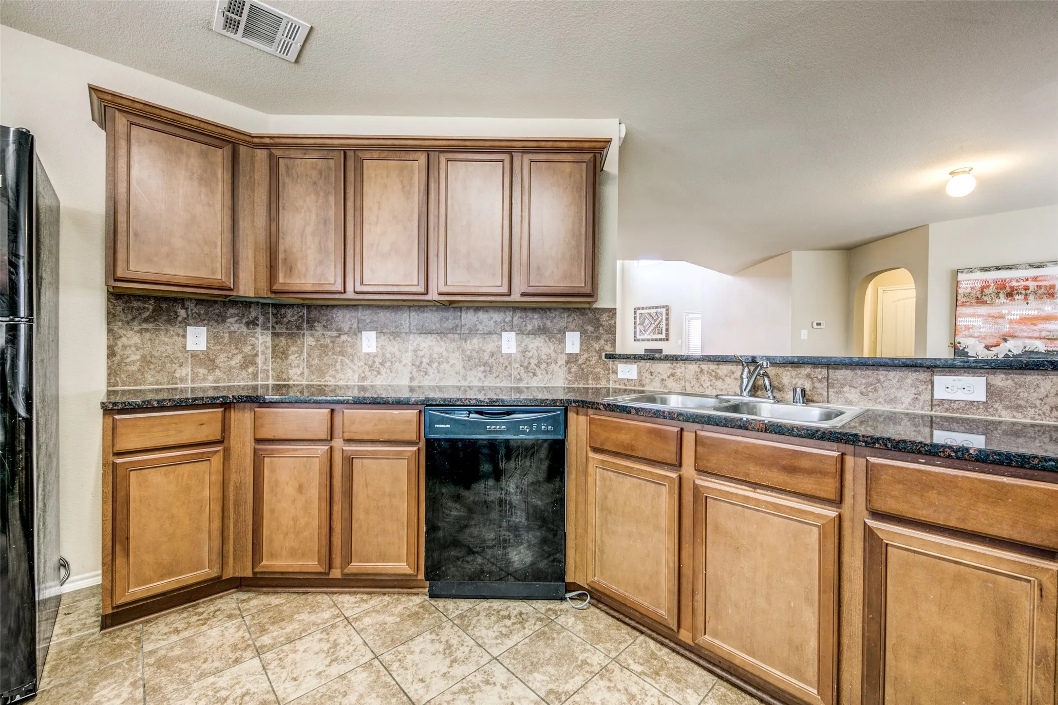 Kitchen featuring wood cabinetry, dark countertops, a tile backsplash, and tile flooring