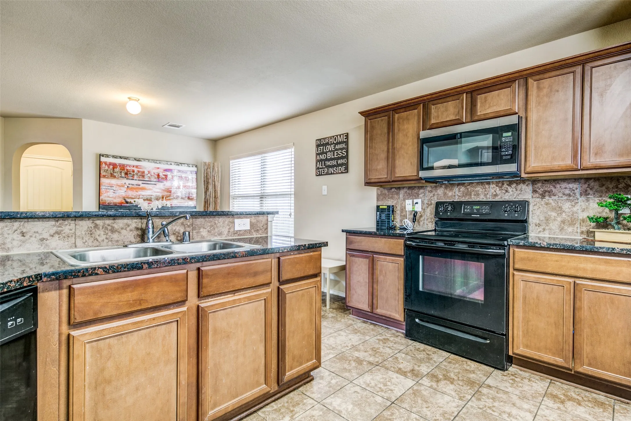 Kitchen featuring wood cabinetry, dark granite-style countertops, and a tile backsplash