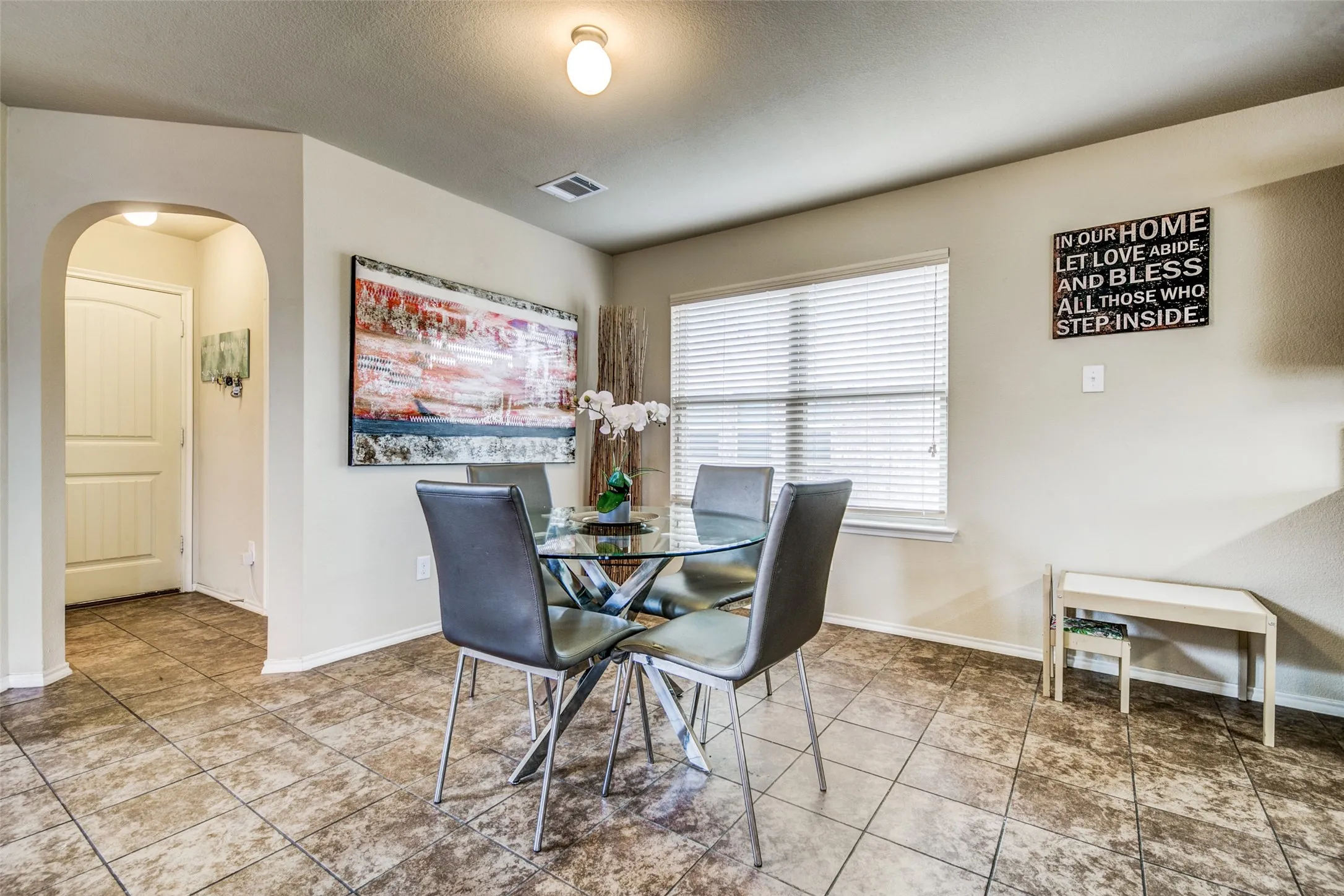 Dining area featuring large-format ceramic tile flooring, a window with horizontal blinds, and a built-in arched doorway