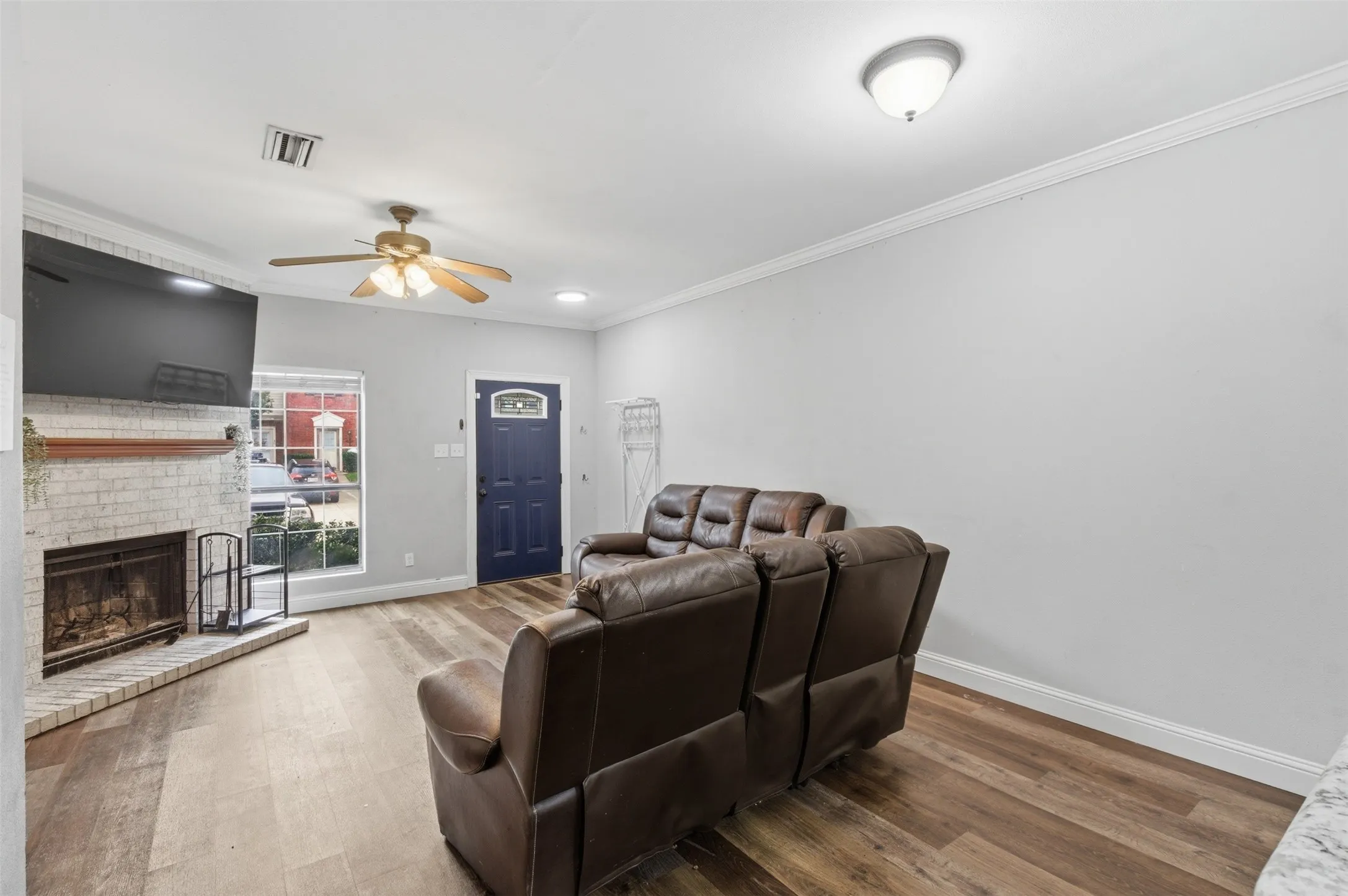 Living area featuring wood-finish flooring, a white brick fireplace with a wood mantle, and a ceiling fan