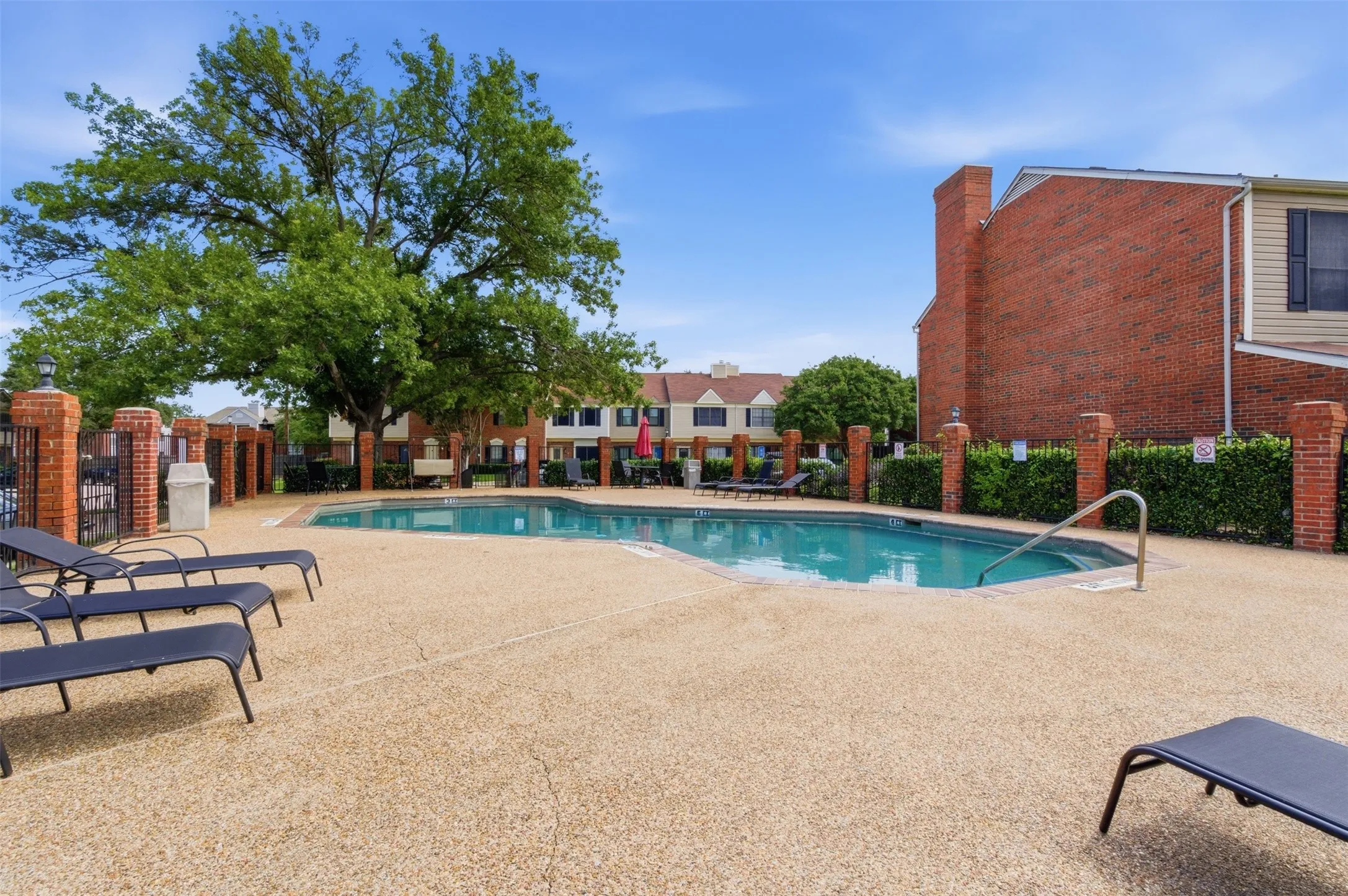 Resort-style swimming pool featuring a textured concrete deck, mature perimeter landscaping, and privacy fencing
