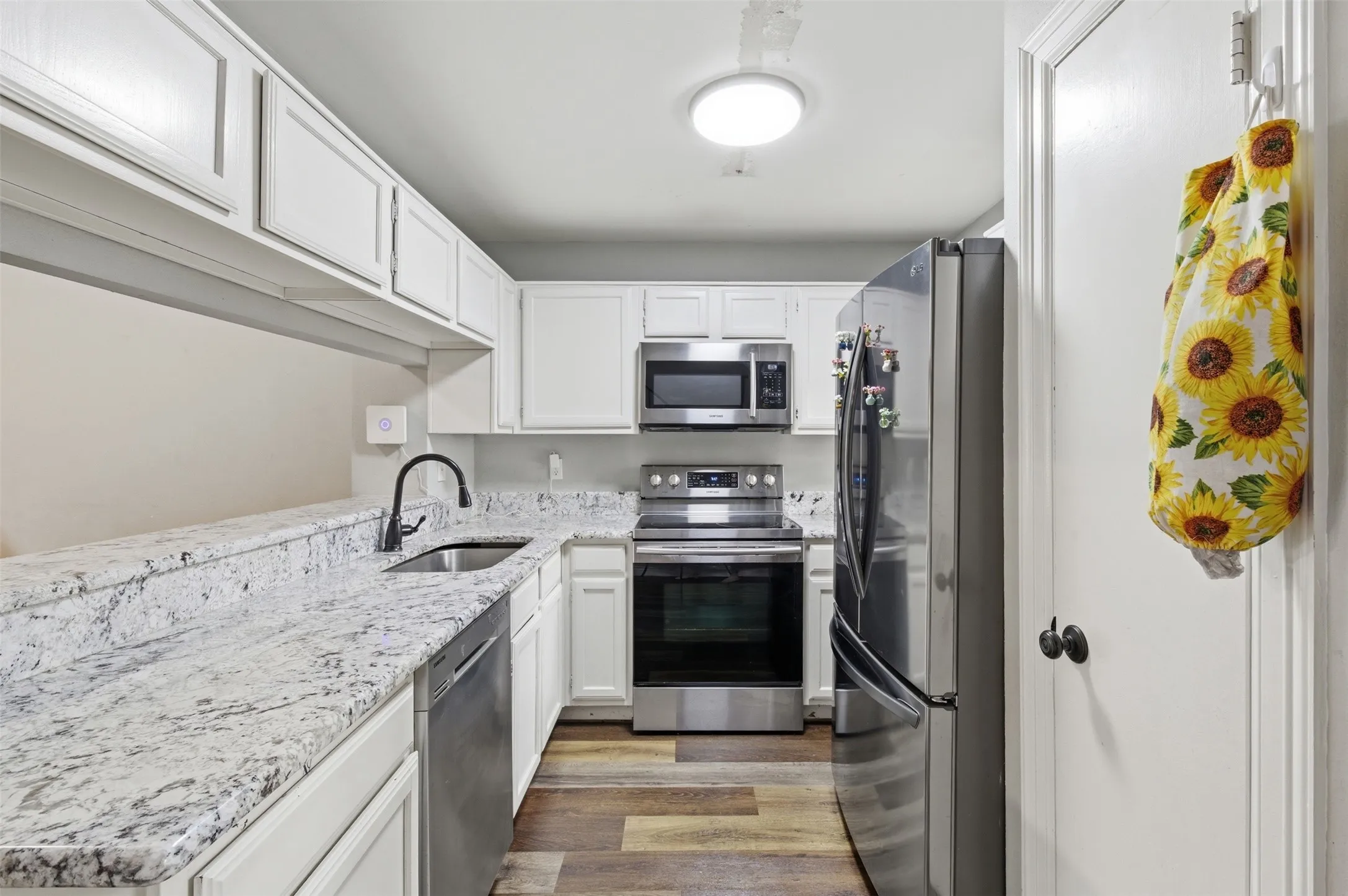 Kitchen featuring white cabinetry, granite countertops, stainless steel appliances, wood-finish flooring, and a modern black faucet