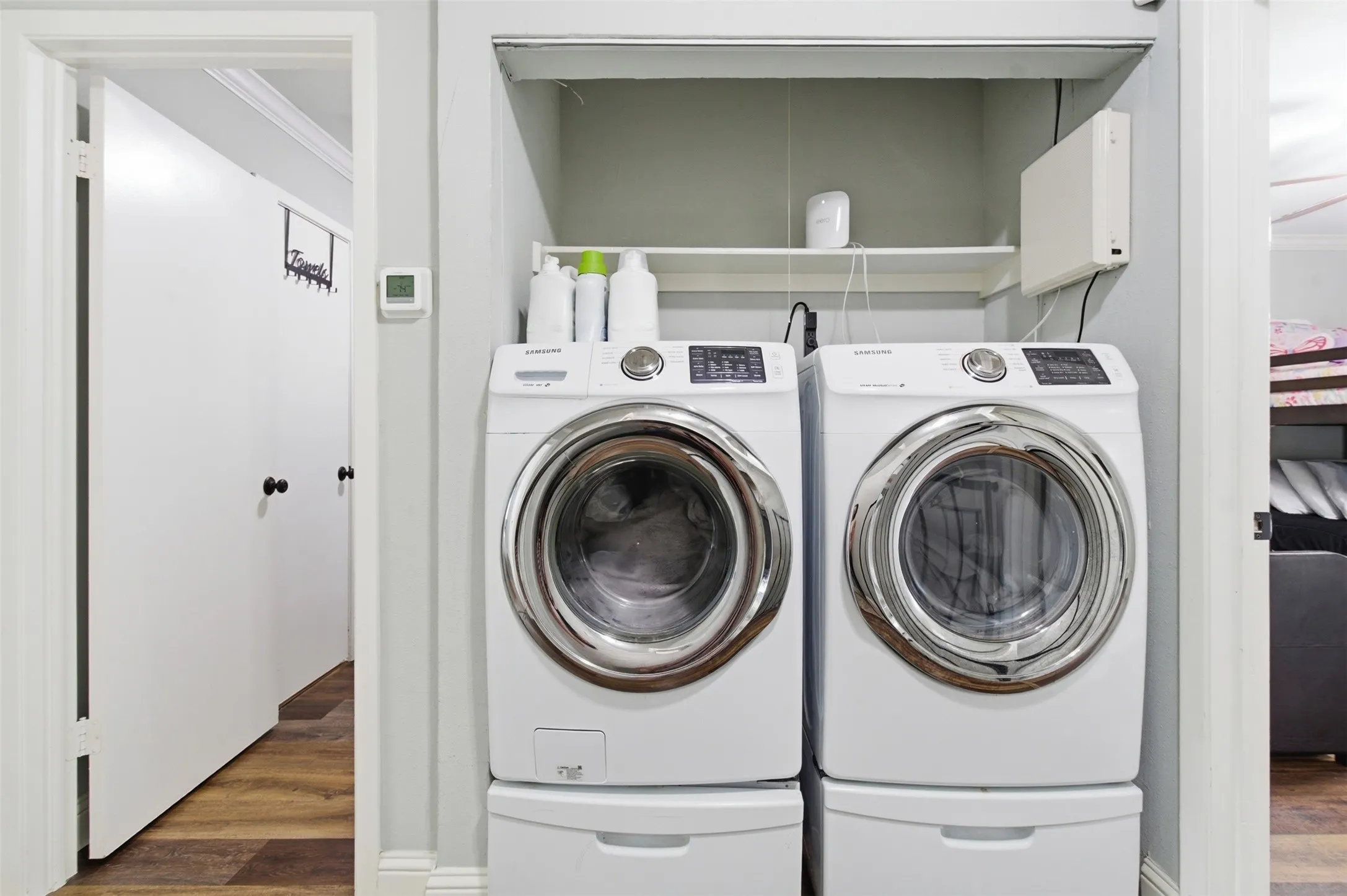 Dedicated laundry area featuring a stacked washer and dryer system with integrated storage pedestals, upper shelving, and recessed lighting