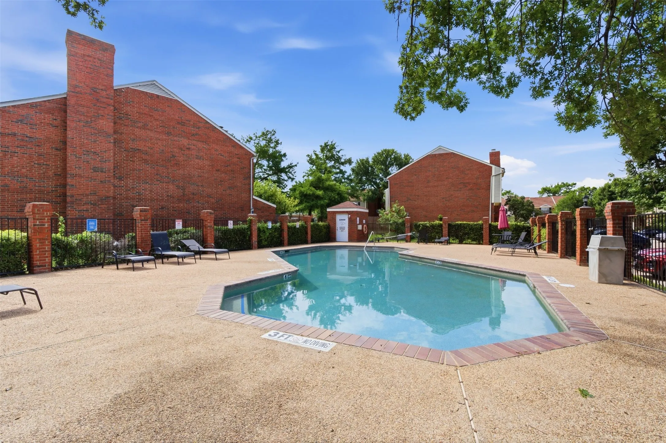Resort-style pool area featuring a perimeter fence, brick-capped pillars, and a surrounding aggregate deck