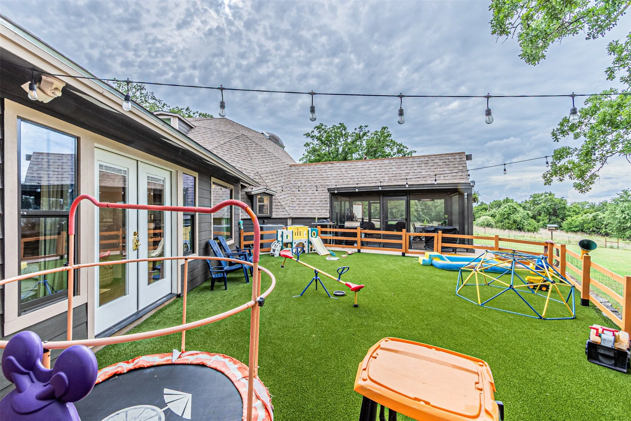 Turfed backyard featuring a screened porch, string lighting, and a wooden fence