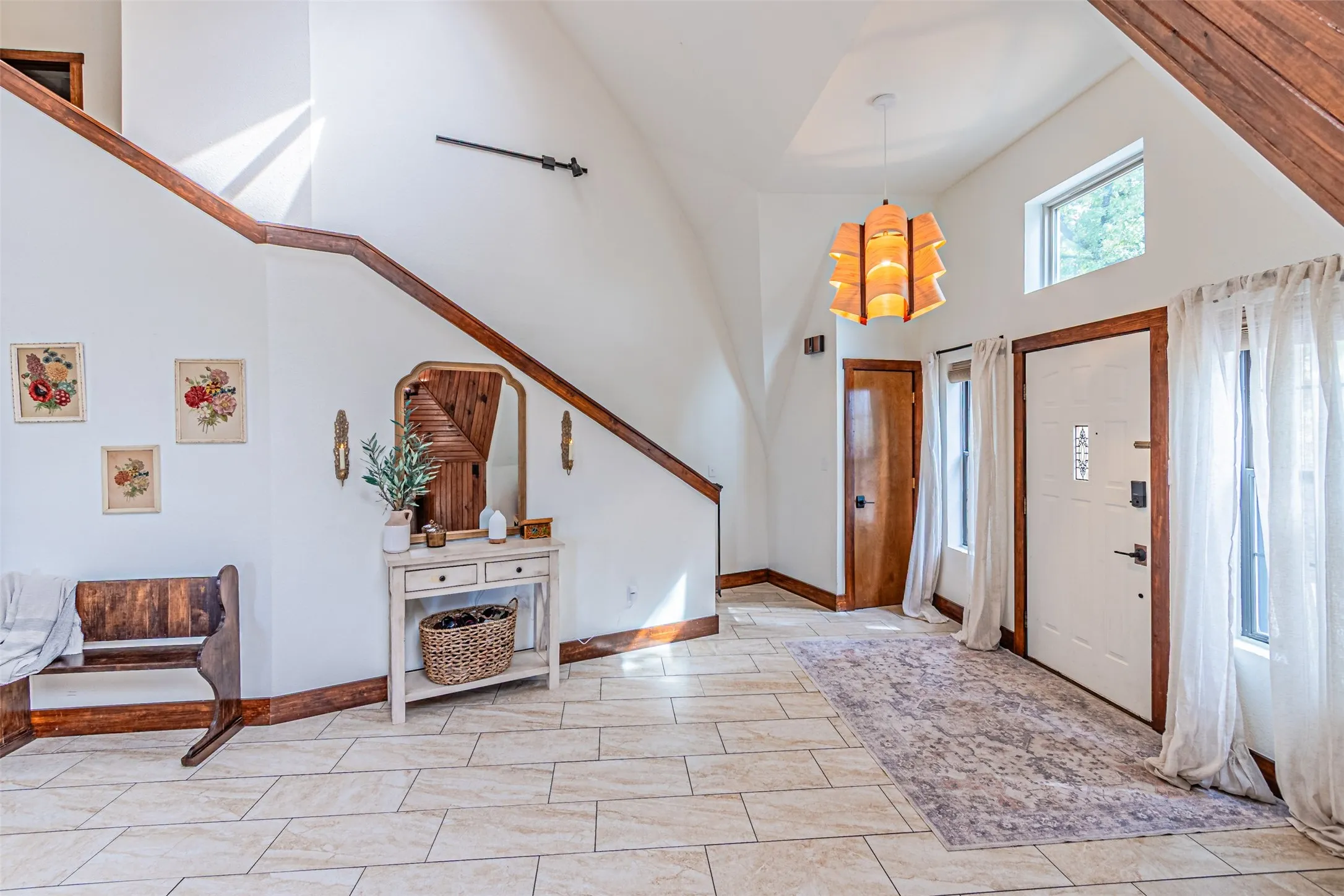 Expansive foyer featuring neutral tile flooring, high ceilings, a prominent staircase with wood trim, a natural wood paneled door, and a white entry door with frosted glass accents