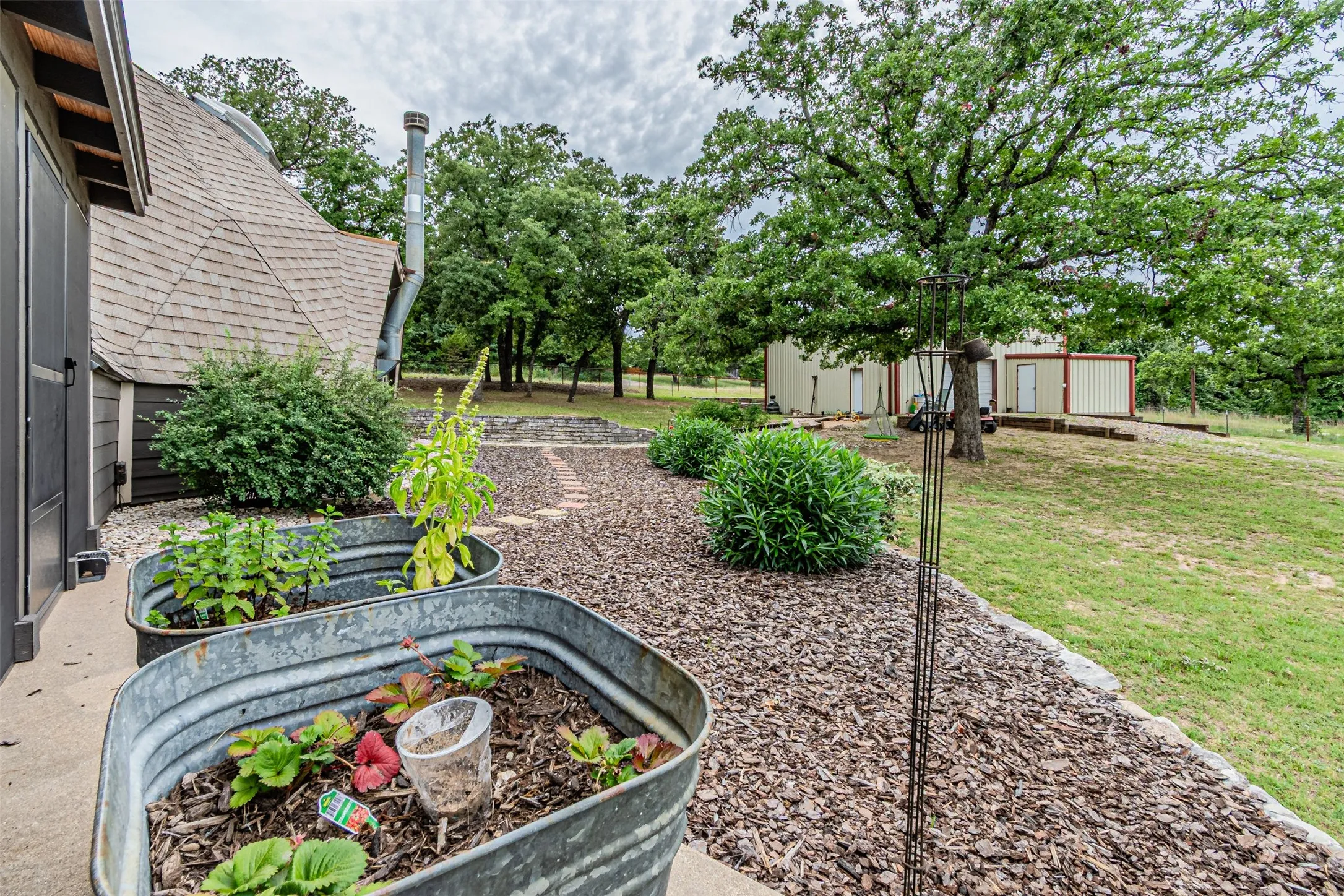 Galvanized planters with varied greenery, gravel landscaping, and a curvilinear stone path