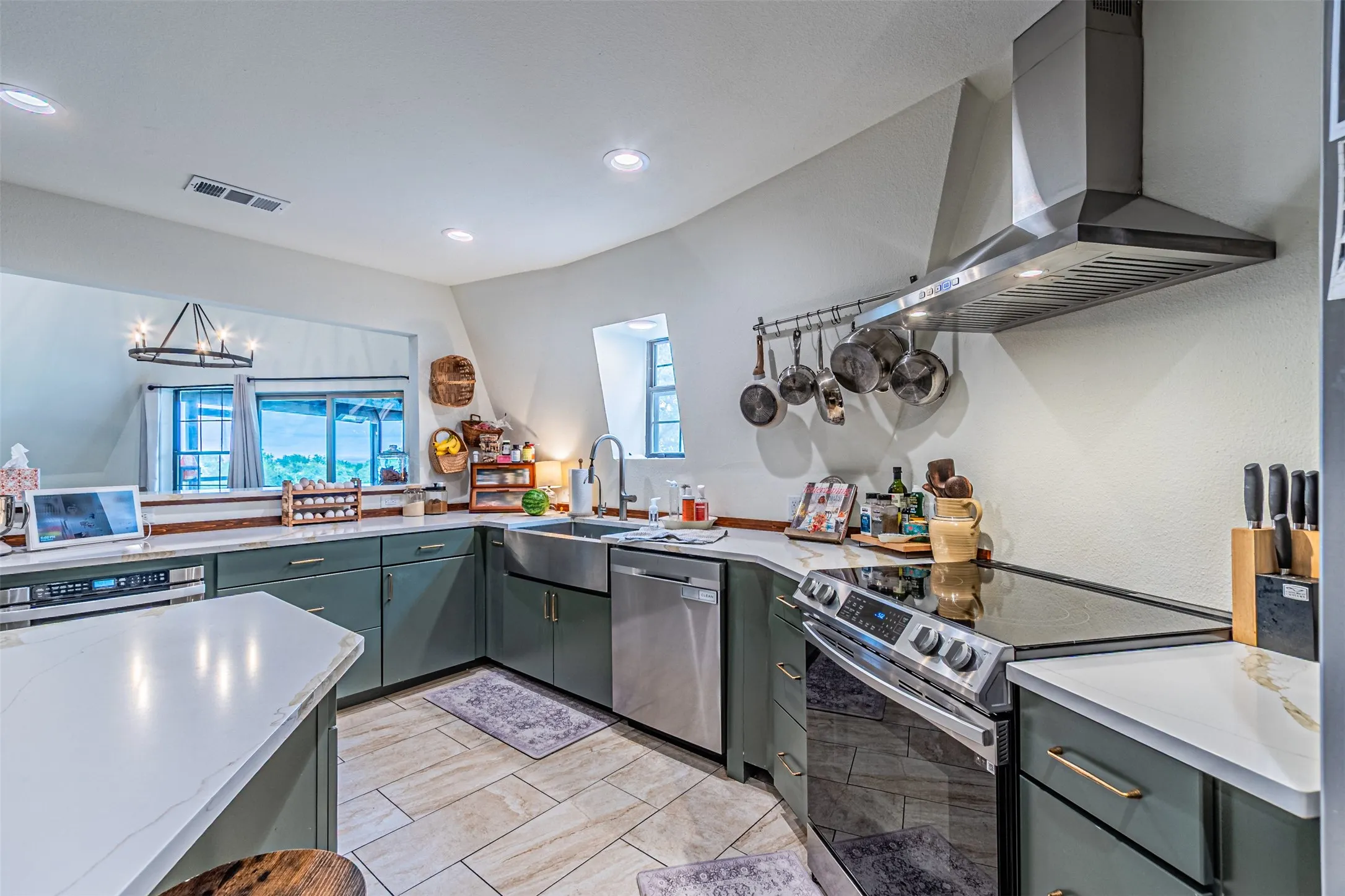 Modern kitchen featuring sage green cabinetry, white stone countertops, stainless steel appliances, and tile flooring