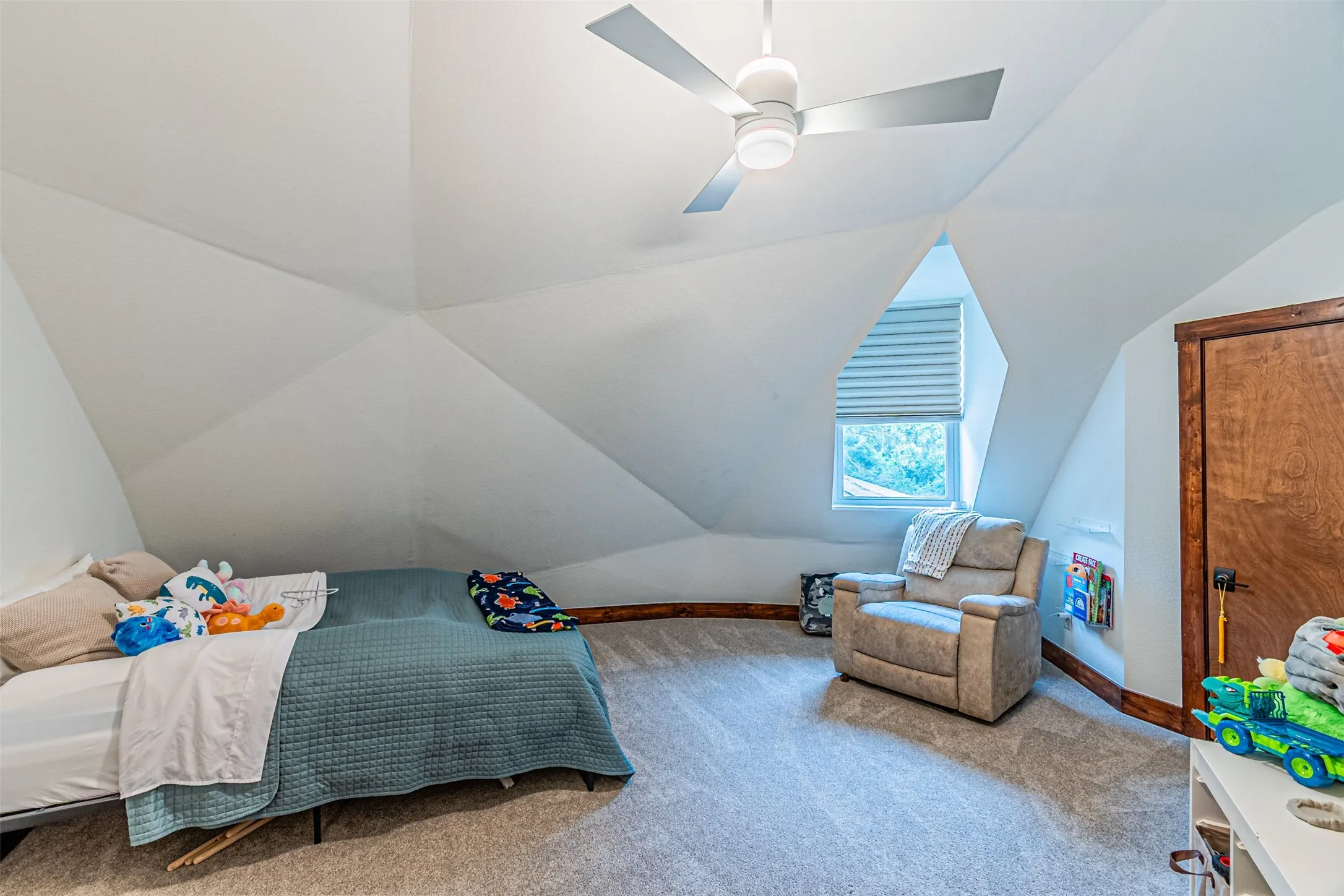 Angled ceiling details with a contemporary ceiling fan, light-colored carpeting, a window with blinds, and rich wood-toned trim
