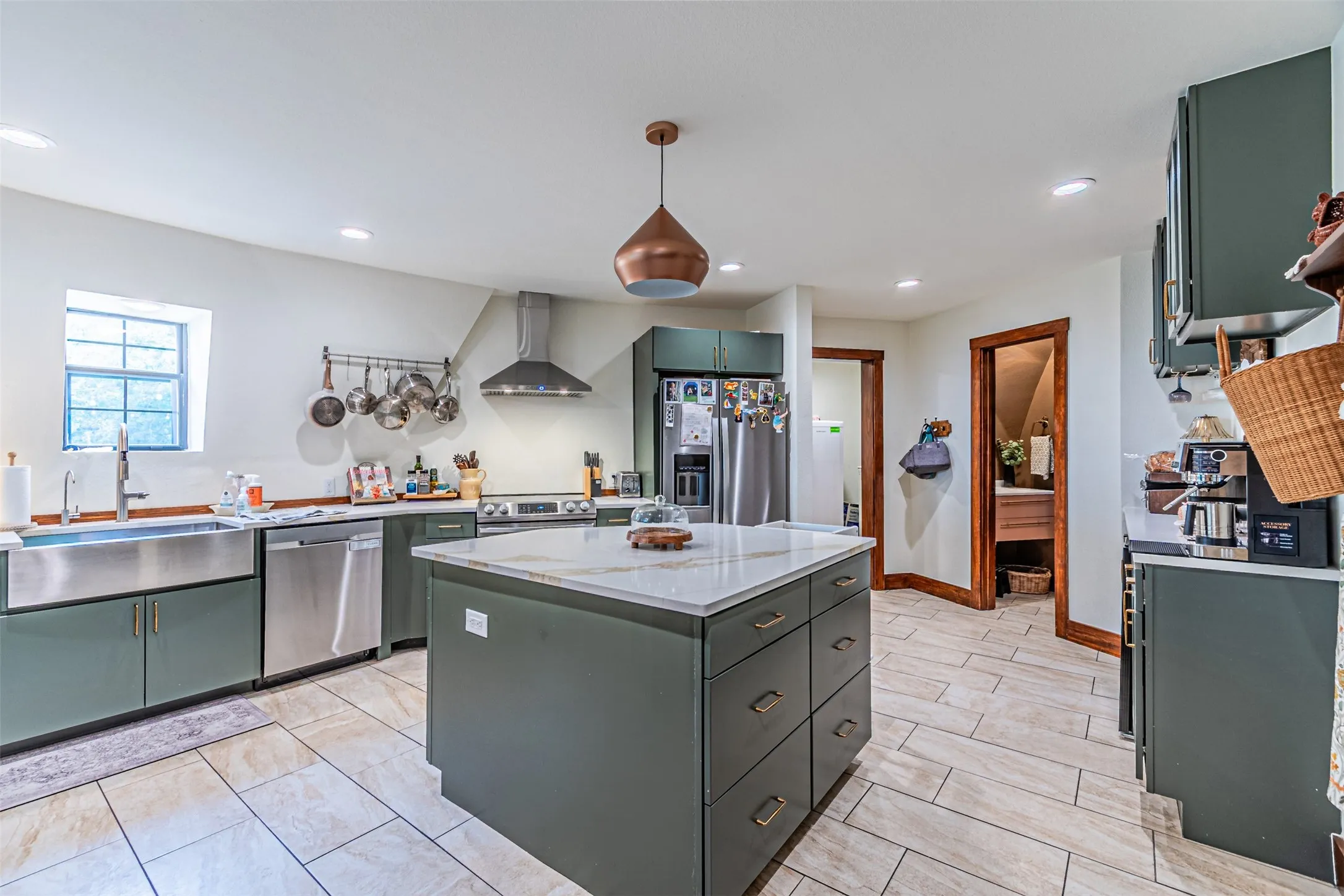 Spacious kitchen featuring an island with a light-toned countertop, stainless steel appliances, olive green cabinetry, a farmhouse sink, and light-toned tile flooring